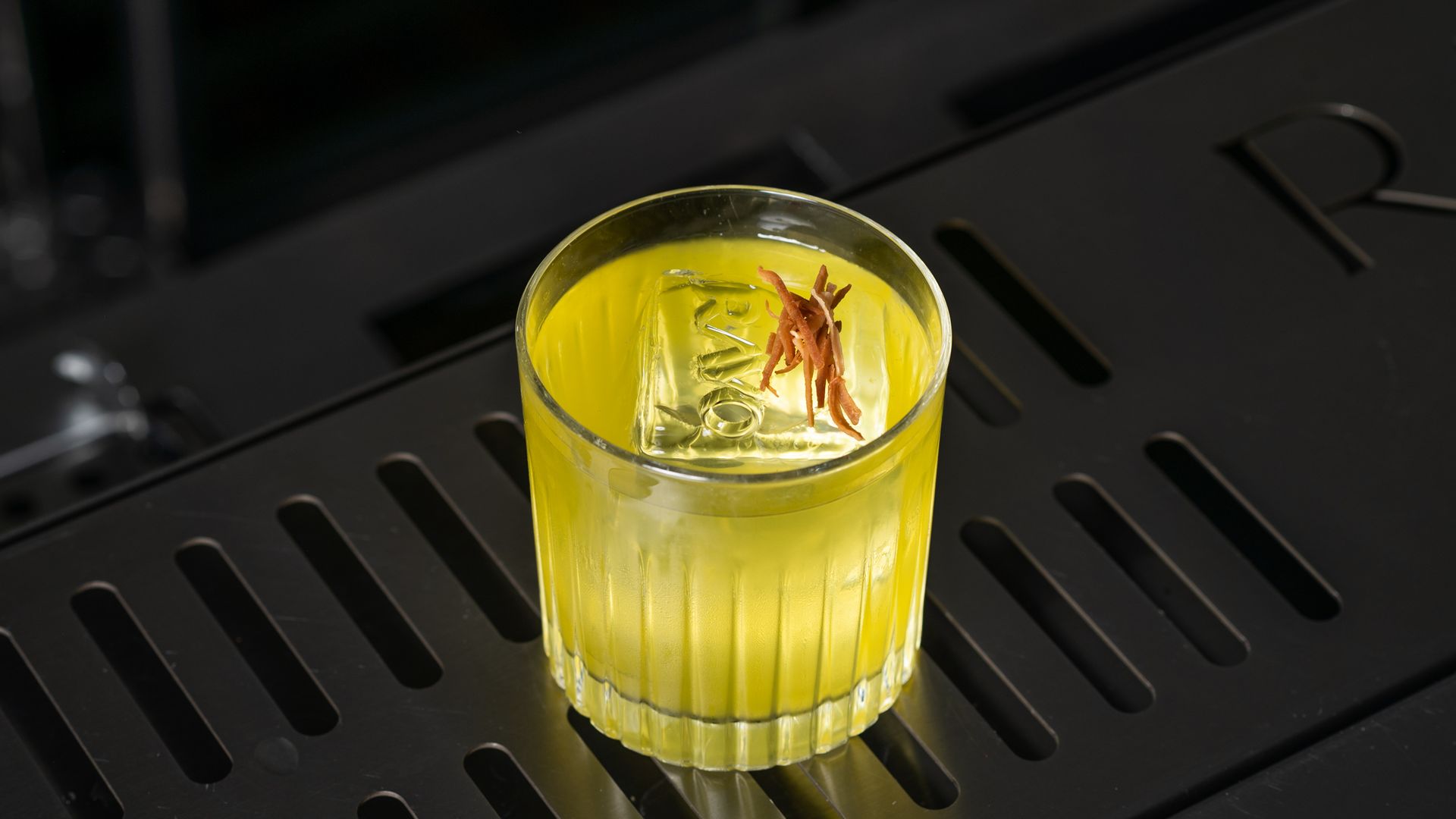 A bright yellow cocktail in a textured glass.