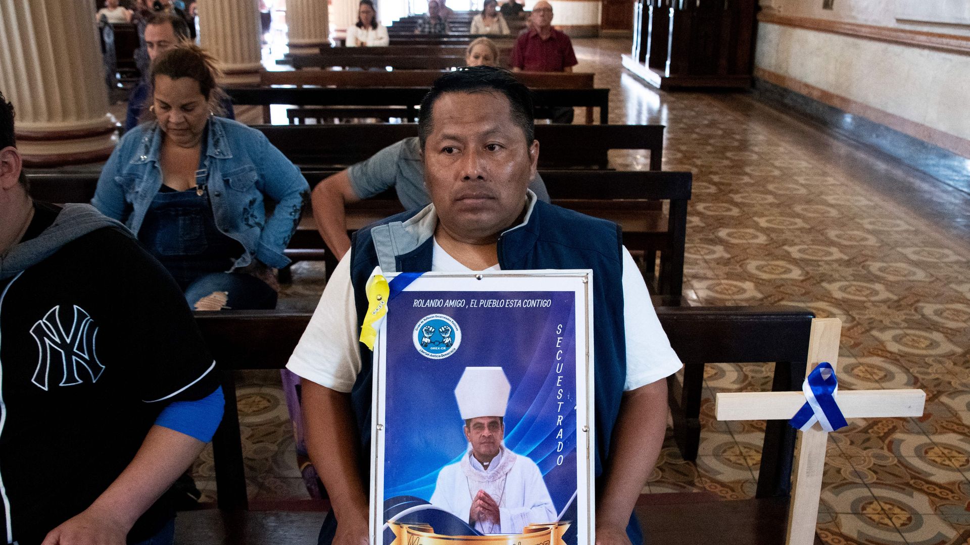 A man sitting on a church pew holds a picture of a Catholic bishop who was exiled from Nicaragua 