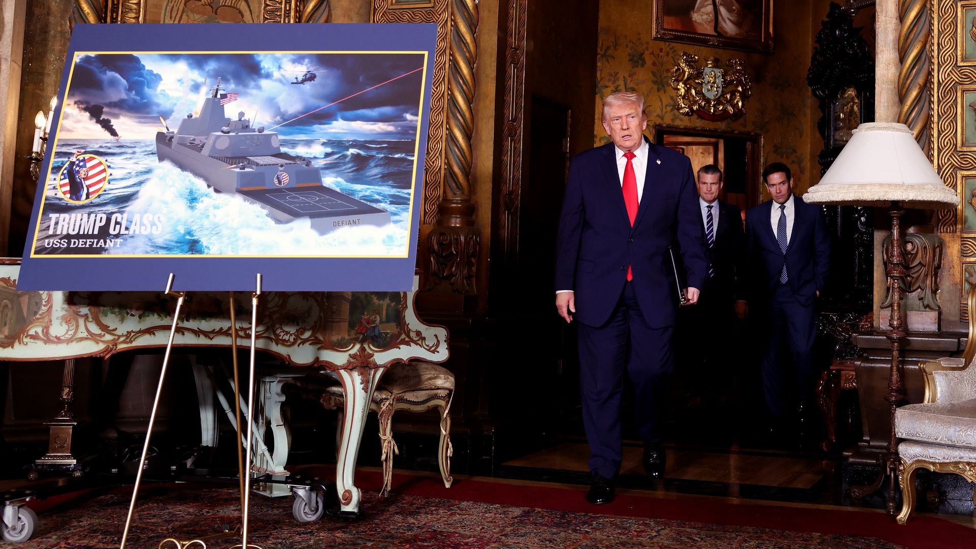 Donald Trump stands in a gold-ornate room beside a large blue poster board showing a sci-fi battleship labeled "Trump Class USS Defiant" firing a red laser across rough seas.