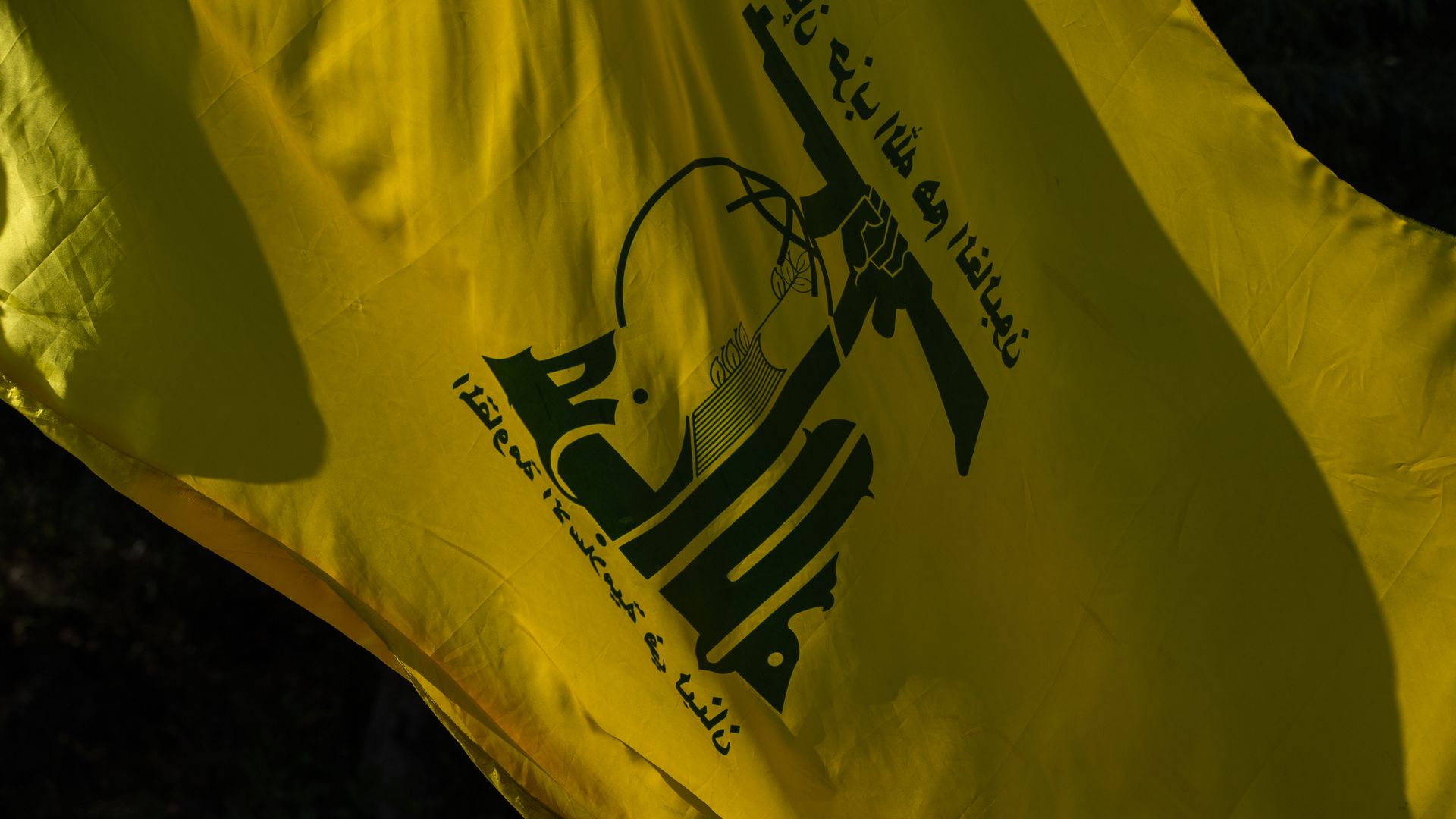 Photo of a yellow Hezbollah flag showing an arm raising a firearm into the sky