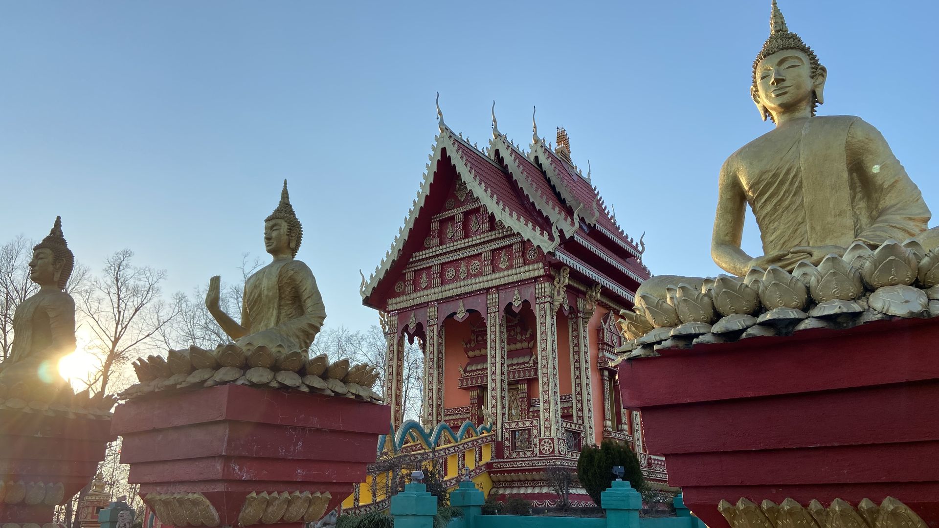 A vibrantly colored Buddhist temple with statues outside during a winter sunset