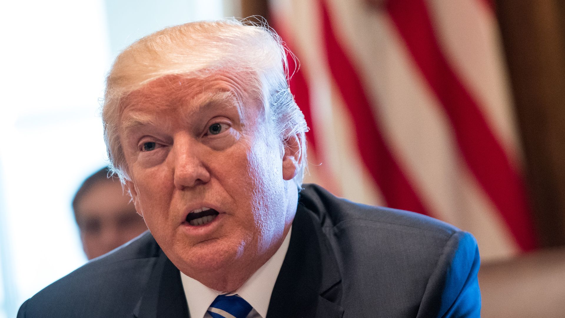 Trump speaks, sitting before an American flag.