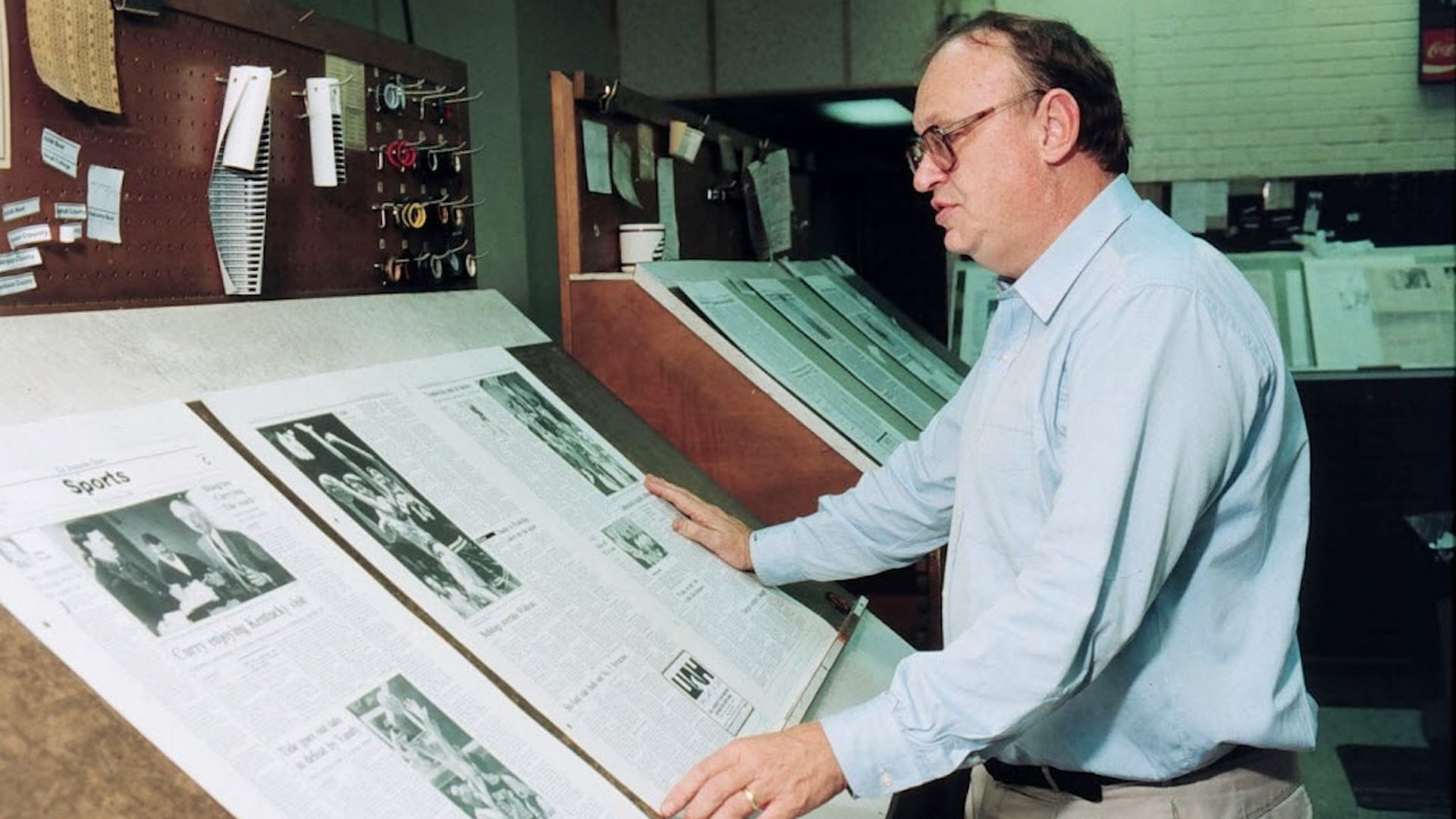 John Pruett, sports writer and editor for the Huntsville Times, stands at a draft table inspecting newspaper pages.