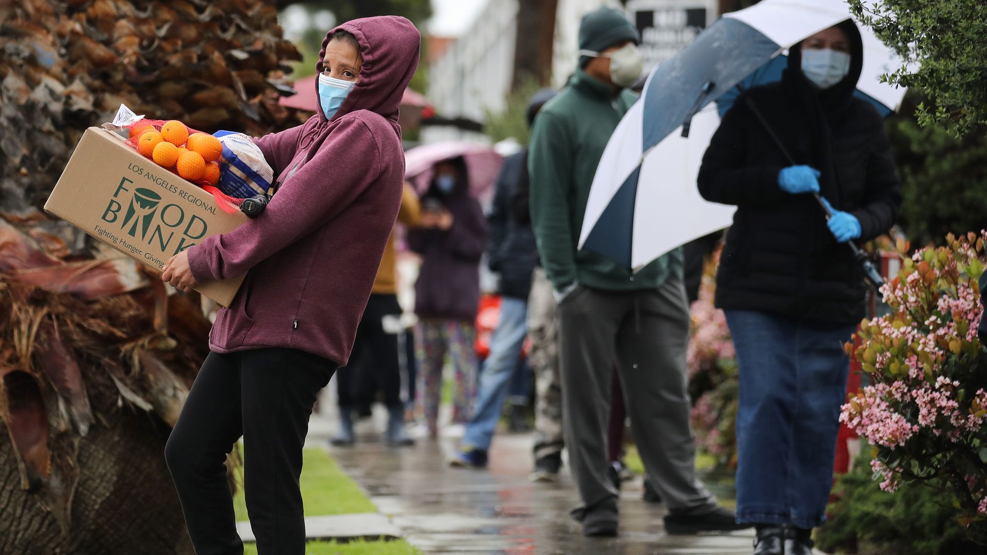A recipient carries a box of food as others wait in line at a Food Bank distribution for those in need as the coronavirus pandemic continues on April 9, 2020, in Van Nuys, California.