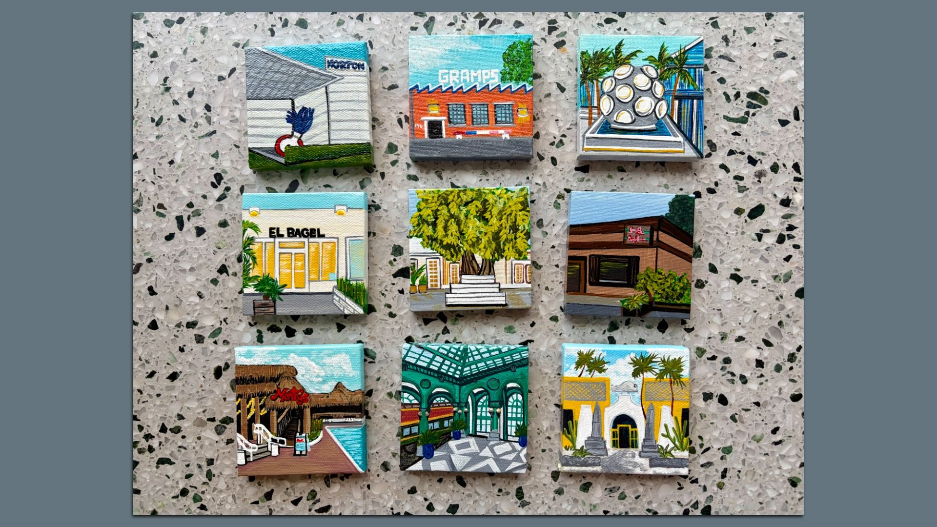 Nine small paintings on a speckled terrazzo floor.