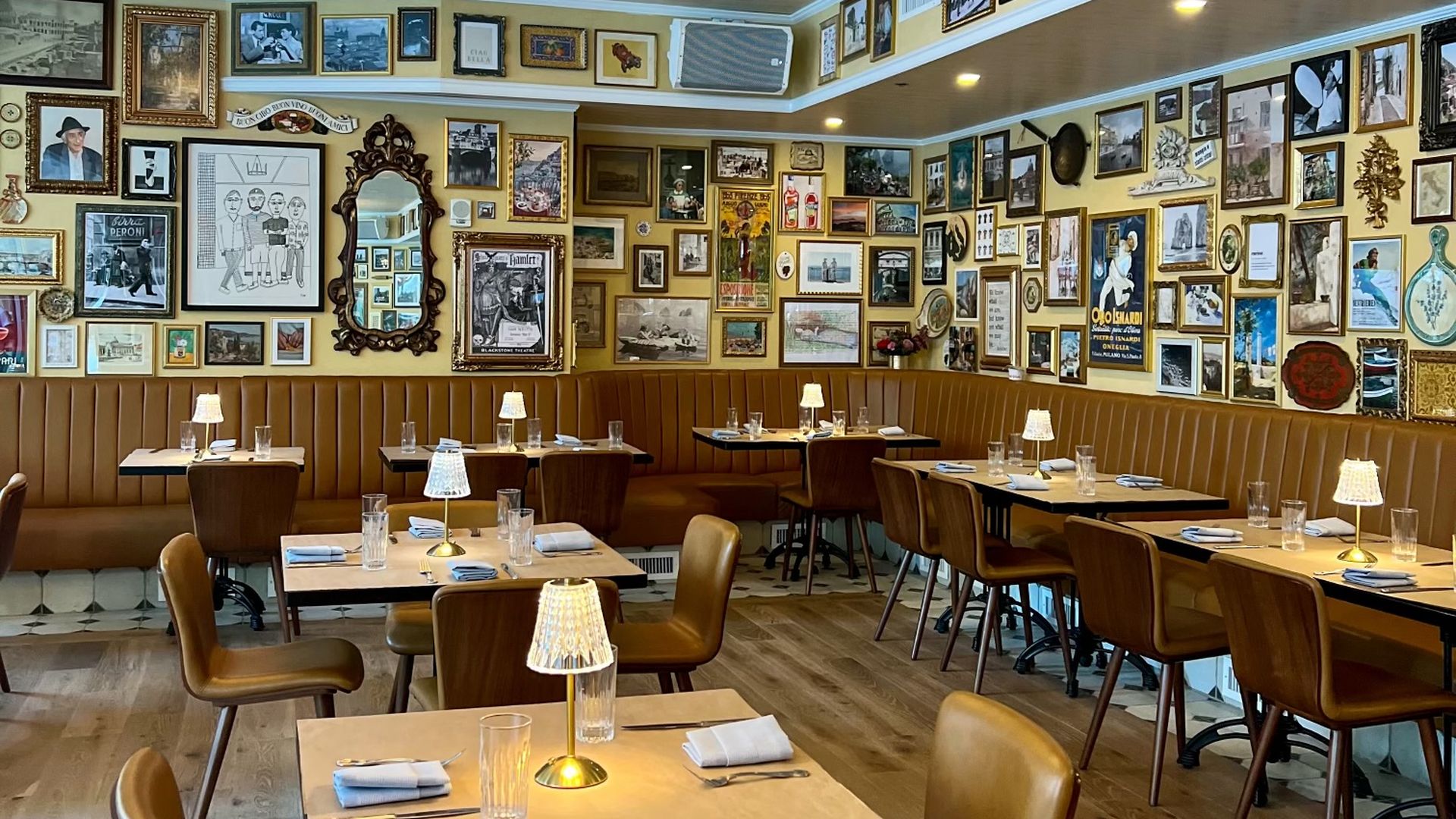 A new pizza place with tables and lots of frames on the wall.