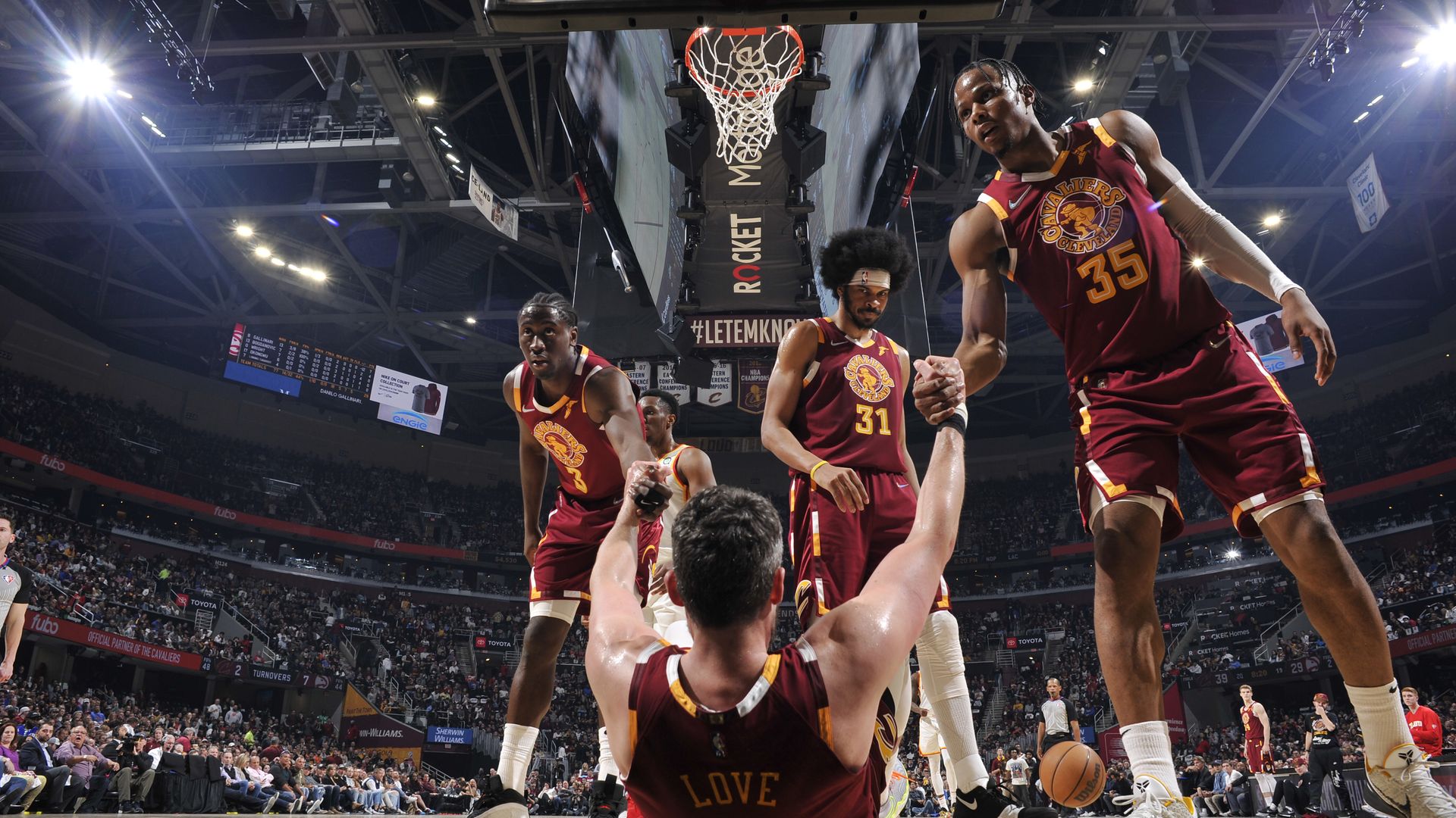 Caris LeVert, Jarrett Allen and Isaac Okoro, in red throwback Cavs jerseys, help Kevin Love stand up from the court