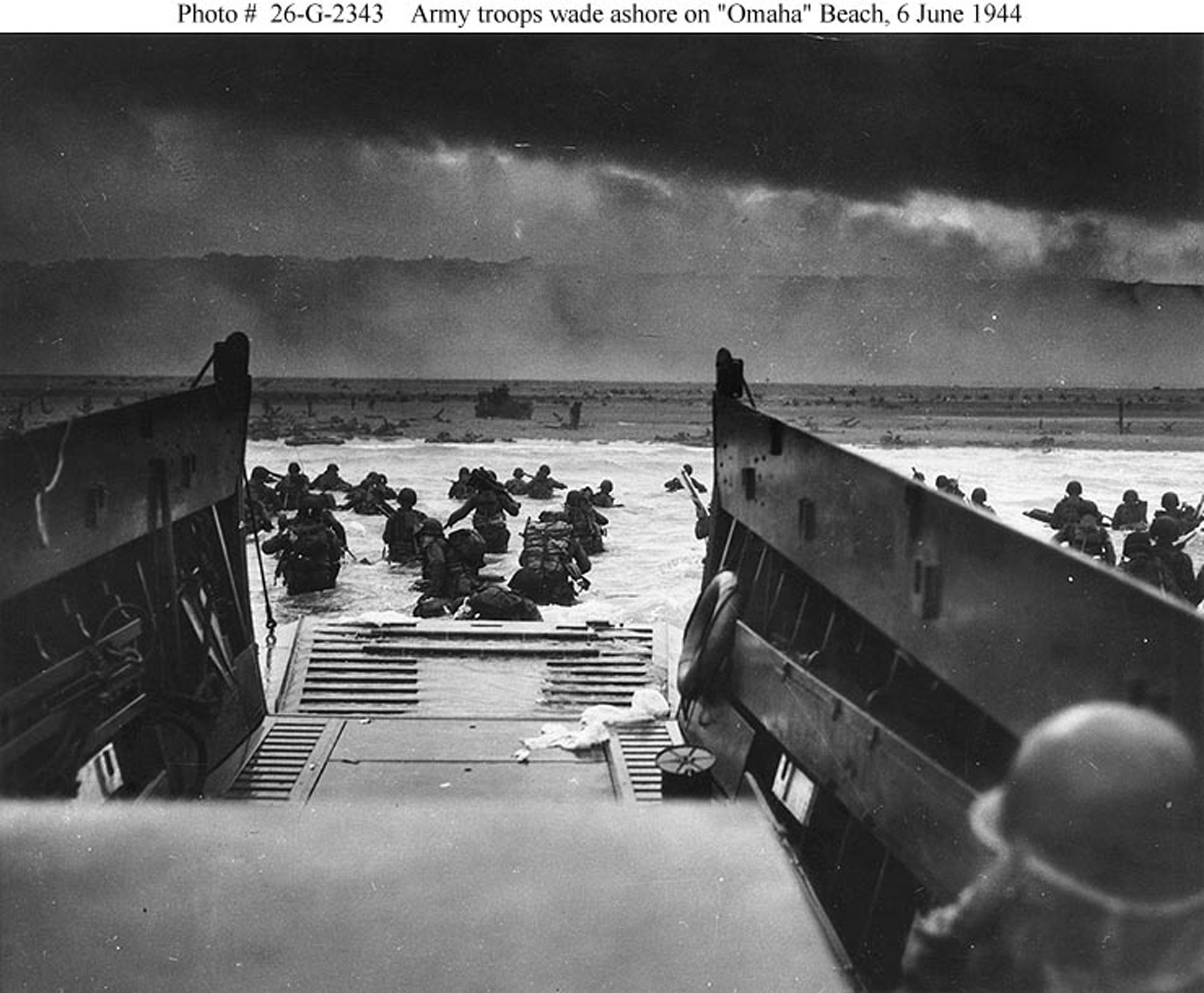 Image shows a black and white photo of troops in the water on D-Day.