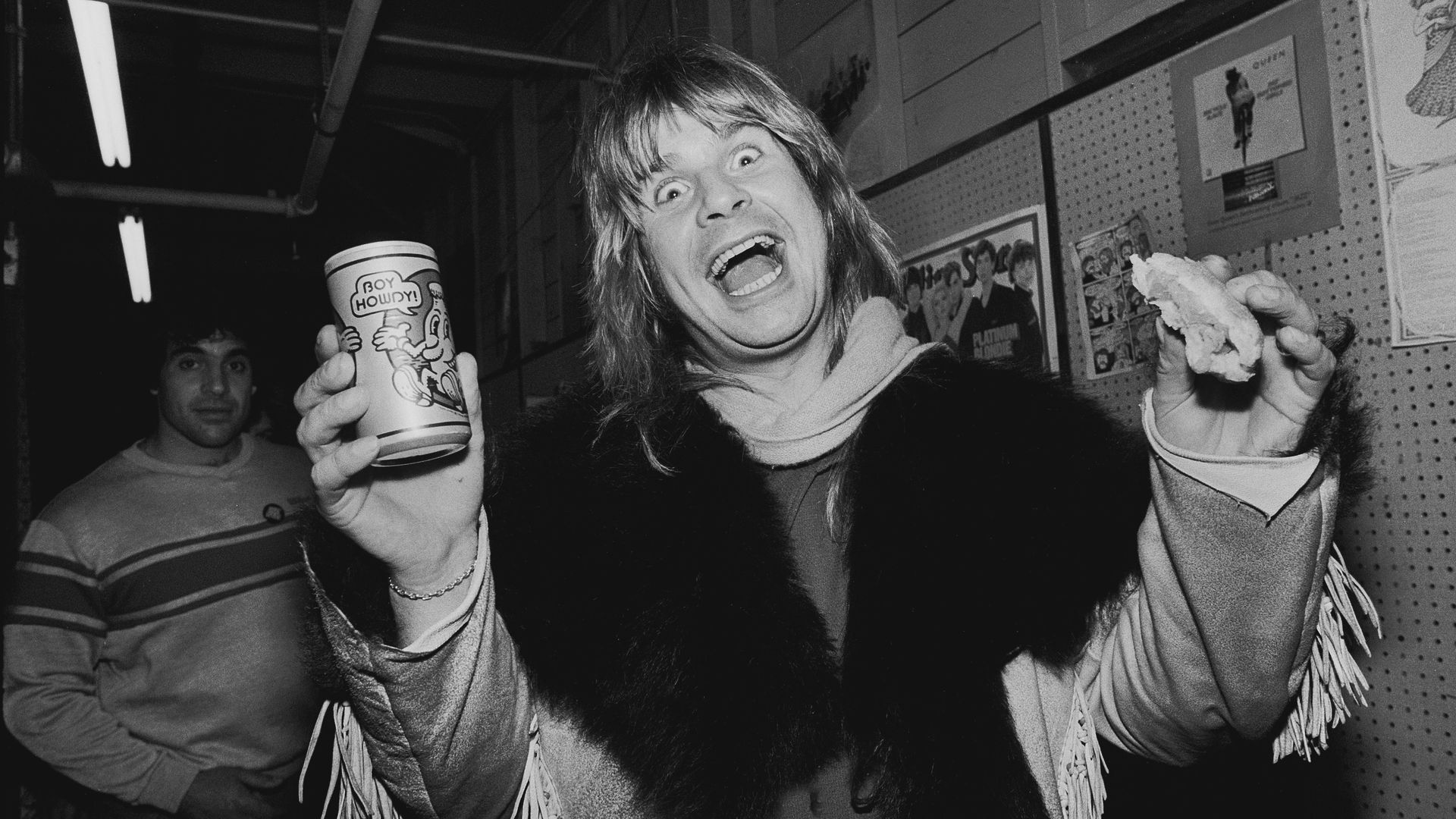 Photo of a man holding a beer and a sandwich while posing for the camera.