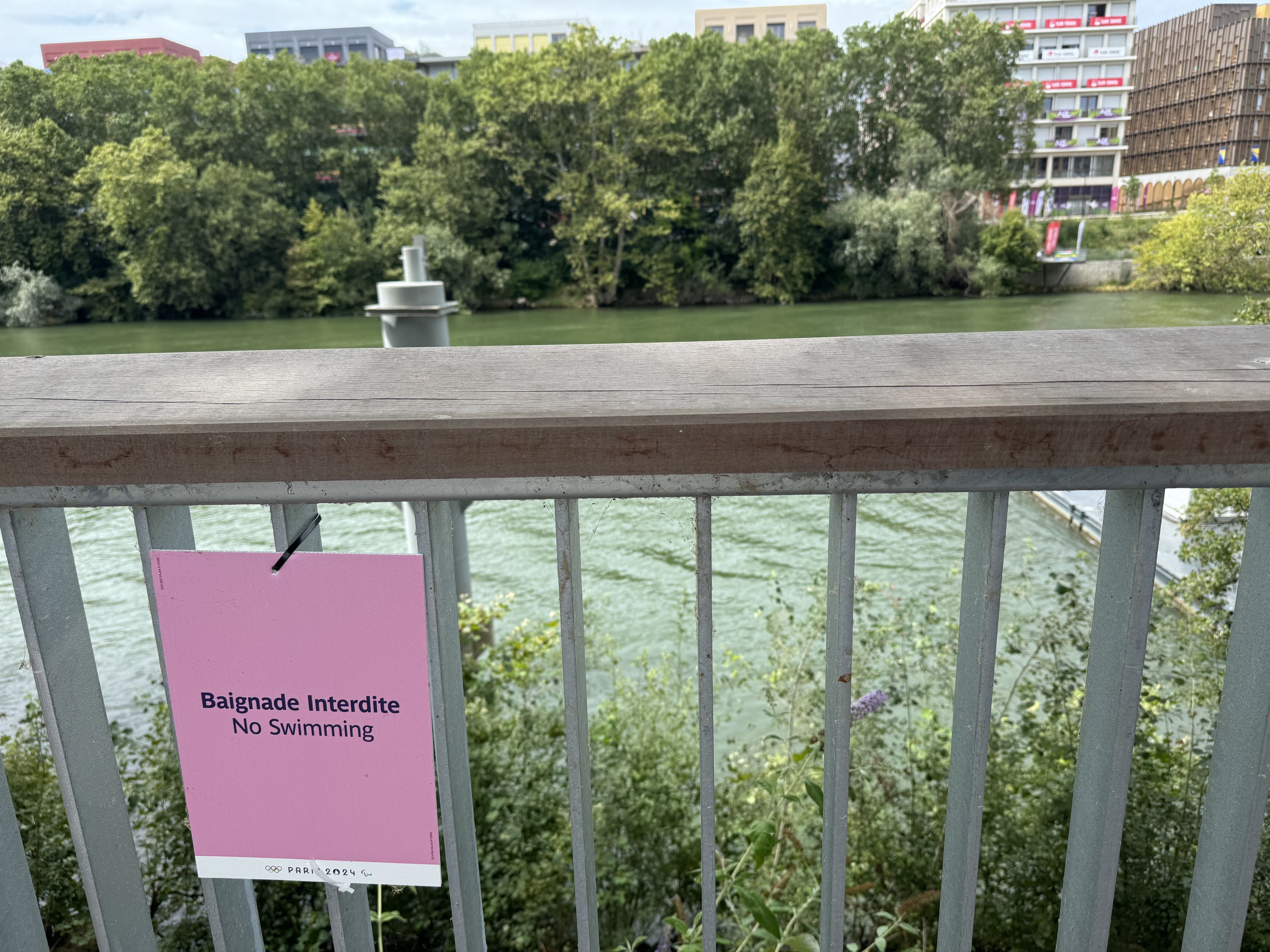 A sign reading "No Swimming" in French and English at the Olympics Village, along the banks of the Seine River.