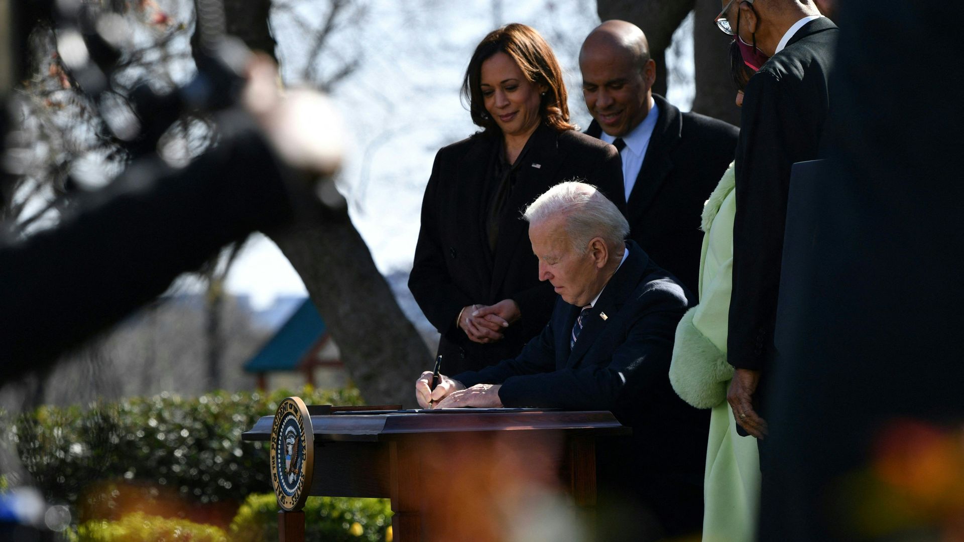 Photo of Joe Biden signing a piece of paper outside the White House with people watching him