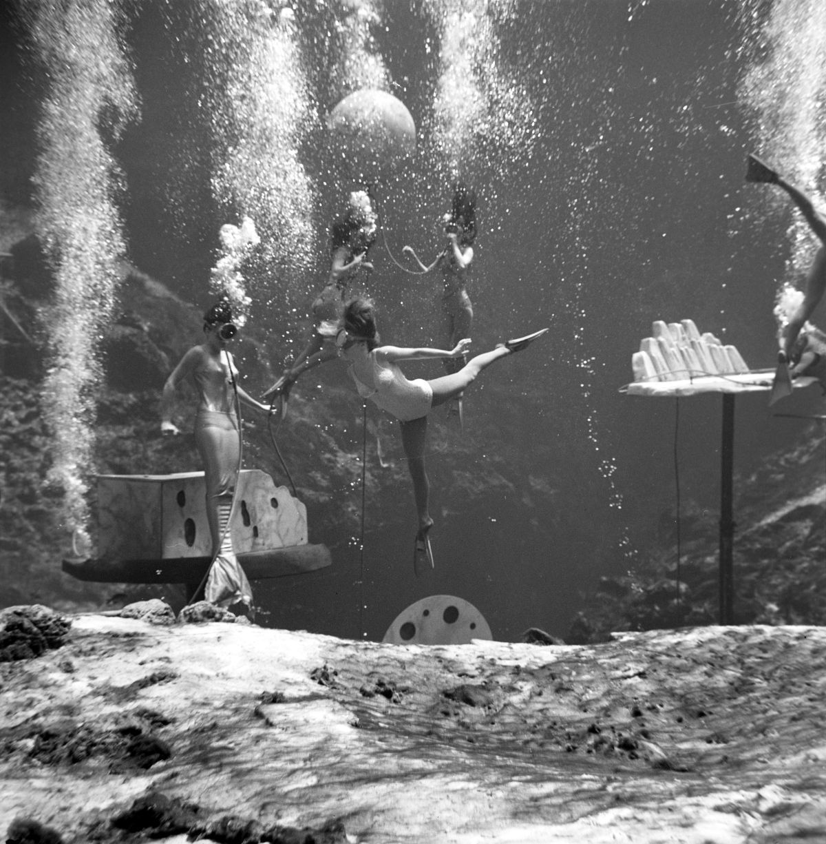 A black-and-white image of several women in bathing suits practicing dance routines underwater.