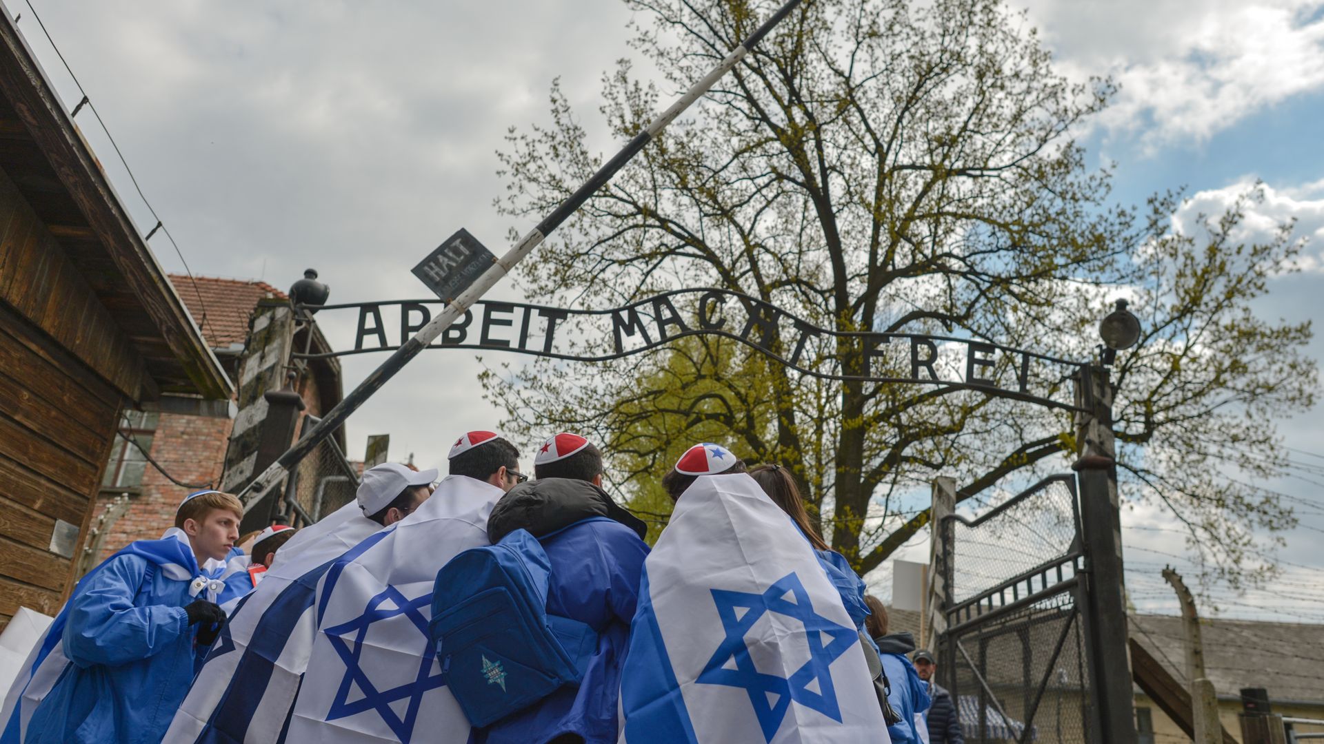 Marchers with Israeli flags on their shoulders stand outside Auschwitz