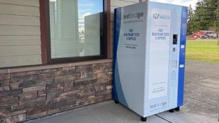 A vending machine containing health products including flu and COVID-19 tests sits outside a building.