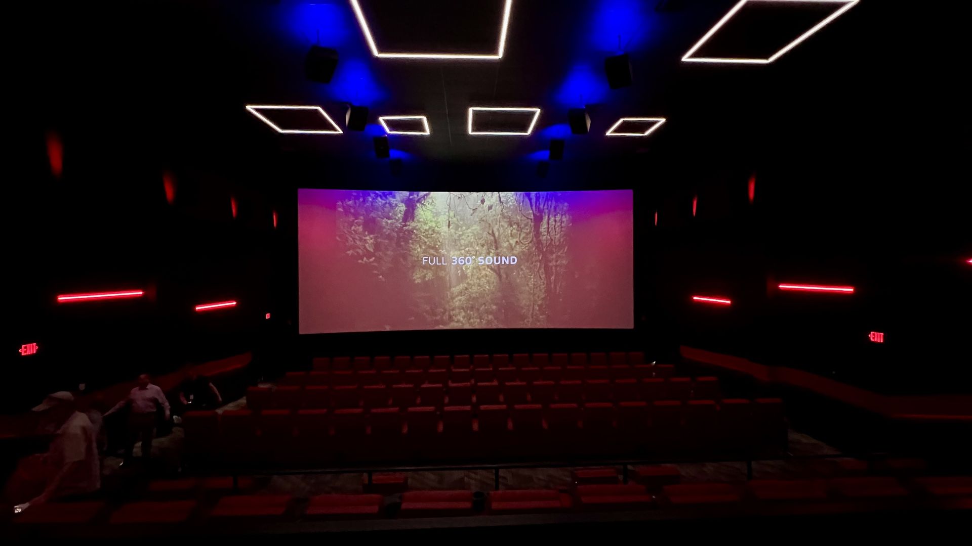 inside a movie theater with red recliners and a wraparound screen
