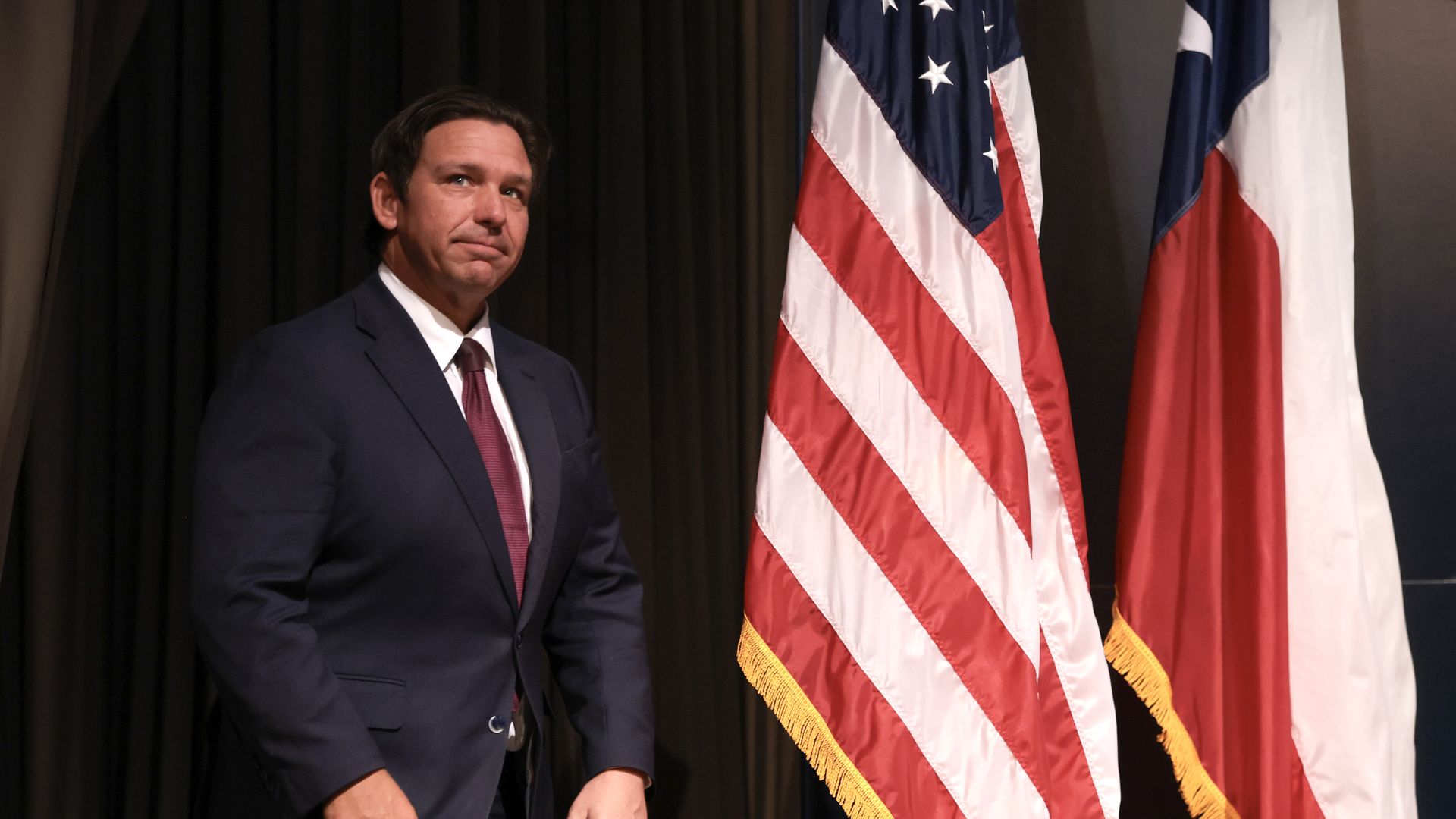 Ron DeSantis stands beside a U.S. flag and a Texas flag.