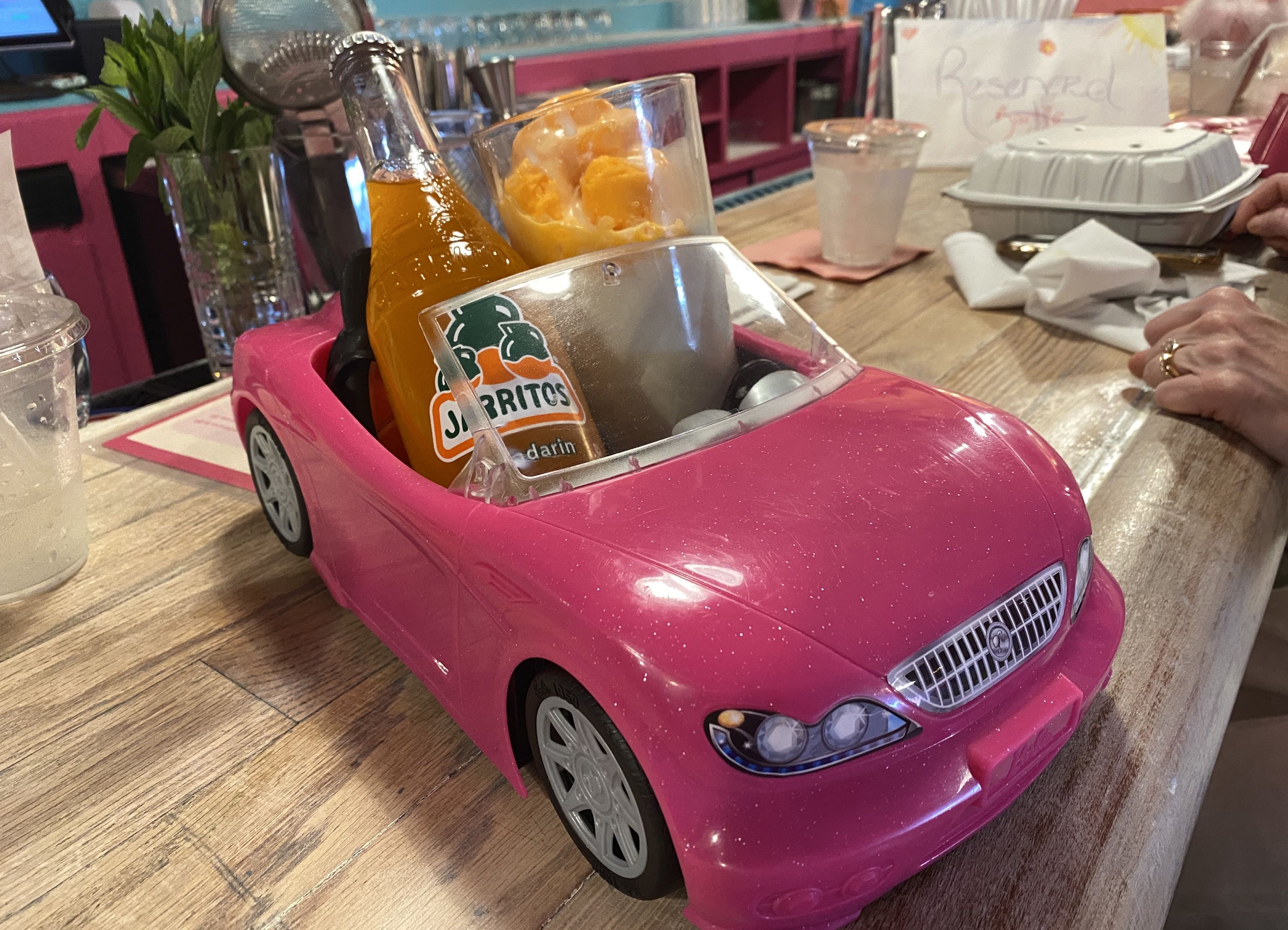 Pink toy car with a Jarritos orange soda bottle and glass of orange ice cream inside.