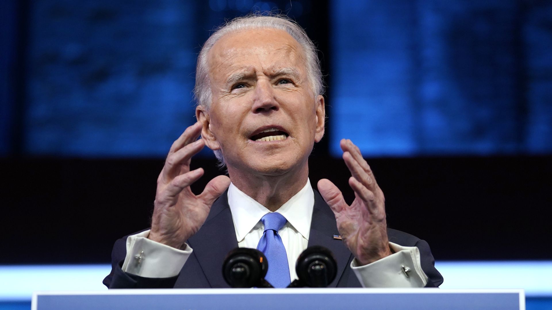 Photo of Joe Biden speaking over a podium with both hands raised