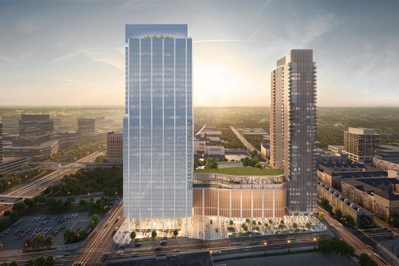 Aerial view of two modern high-rise buildings at sunset in an urban area, with glass facades, green rooftop, busy streets, and cityscape extending into the horizon.