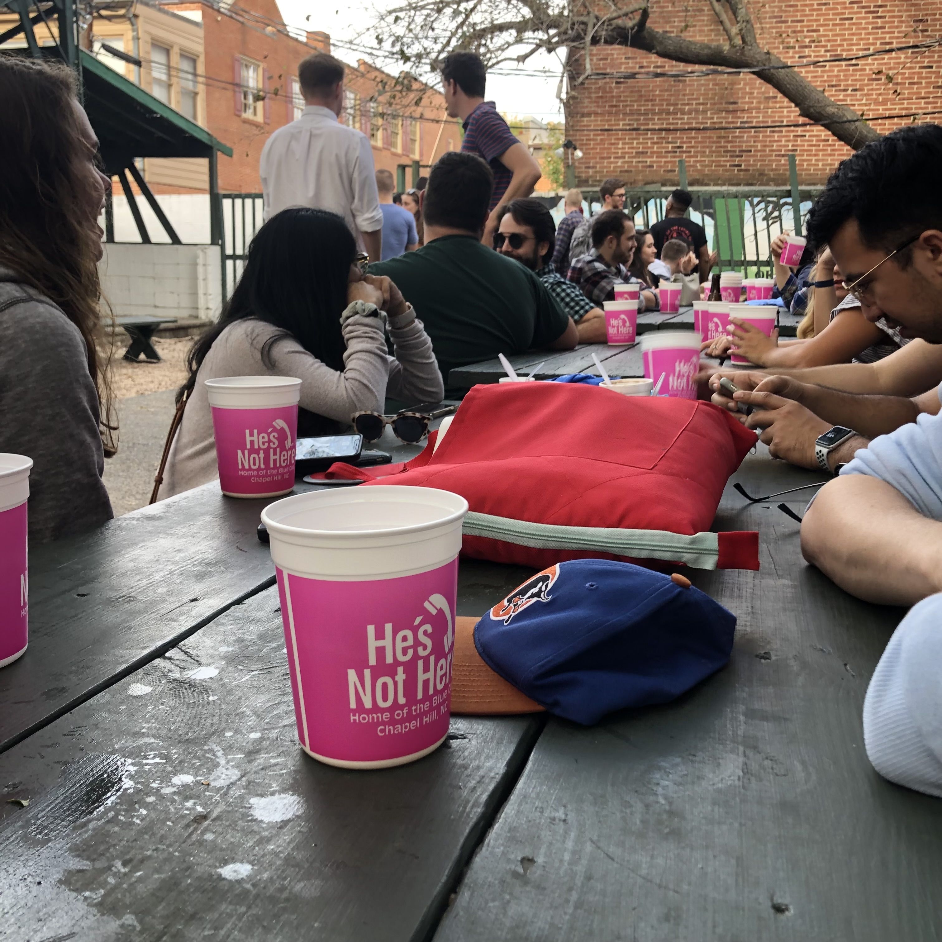 A table with pink He's Not Here cups all over it