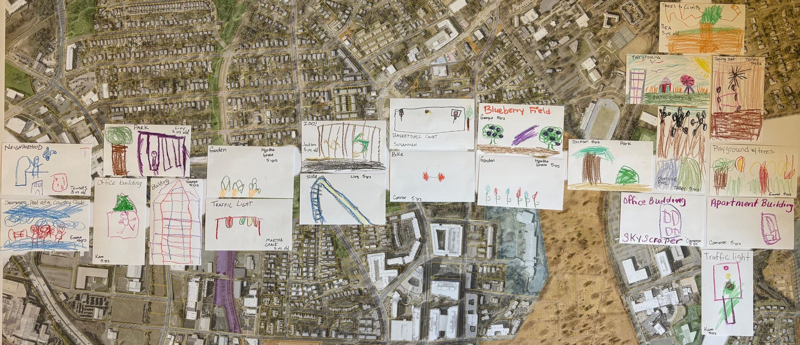 An aerial neighborhood map overlaid with many child-drawn cards showing parks, playgrounds, schools, and buildings in bright crayons.