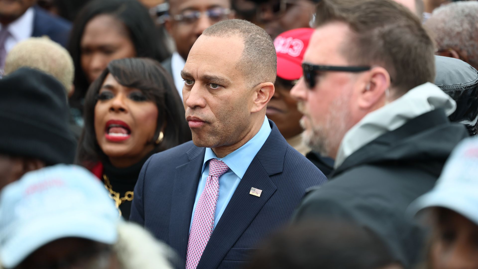 House Minority Leader Hakeem Jeffries, wearing a blue suit and surrounded by colleagues and others.