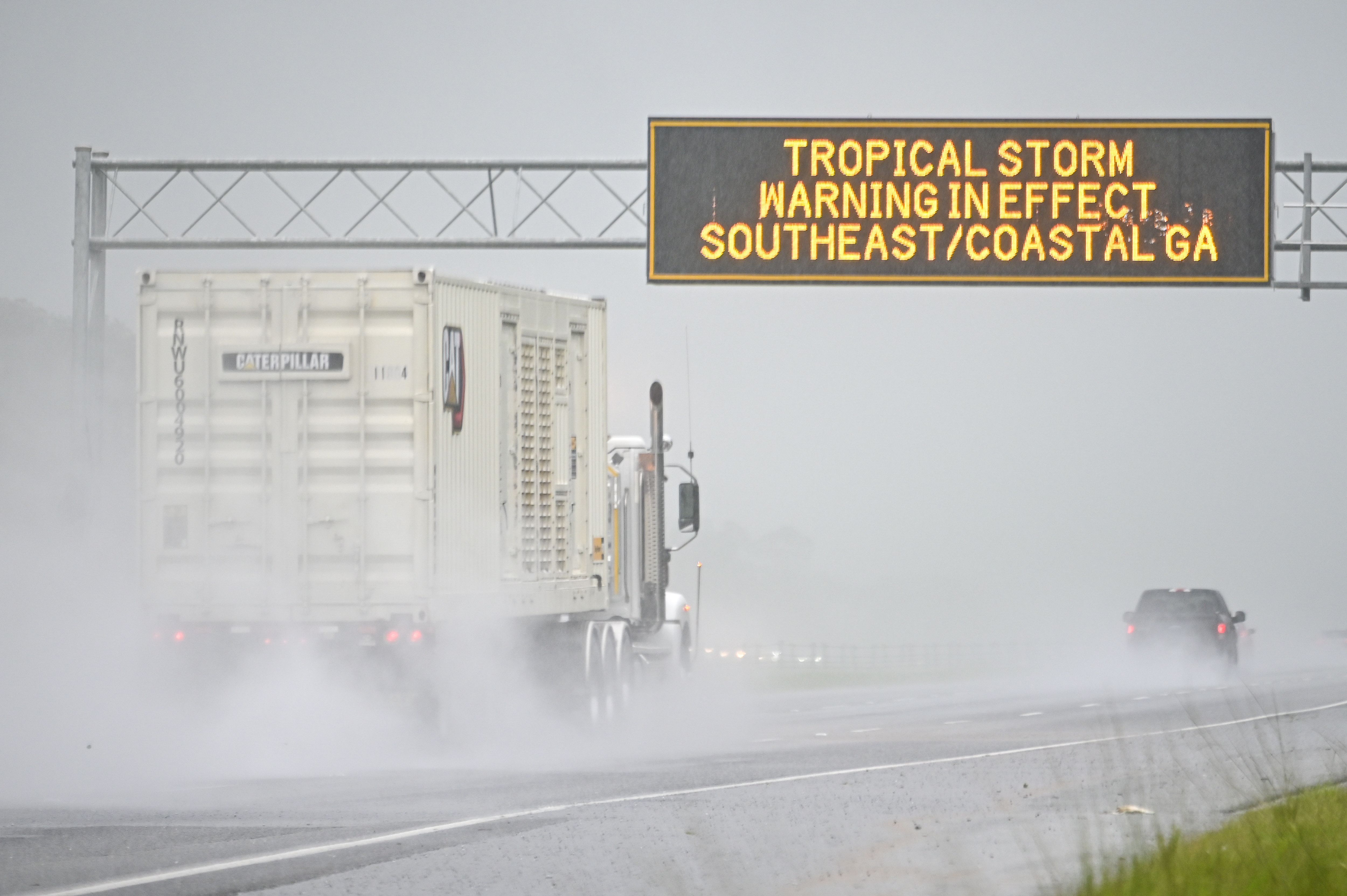 A truck drives under a sign on the road that reads "tropical storm warning in effect southeast/coastal GA"