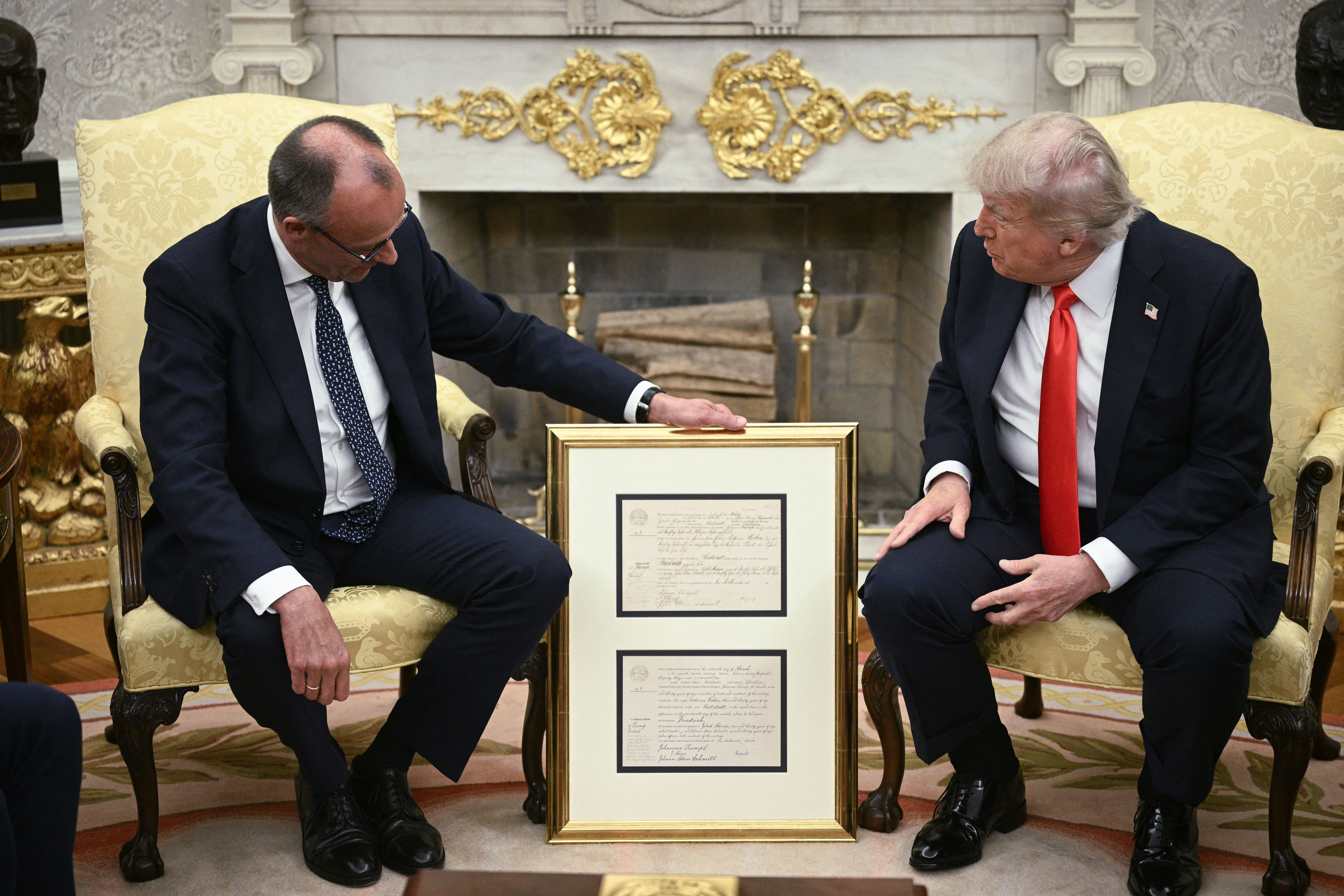 川普身穿藍色西裝、白色襯衫和紅色領帶，默茨身穿藍色西裝、白色襯衫和藍色花紋領帶，手持出生證明。