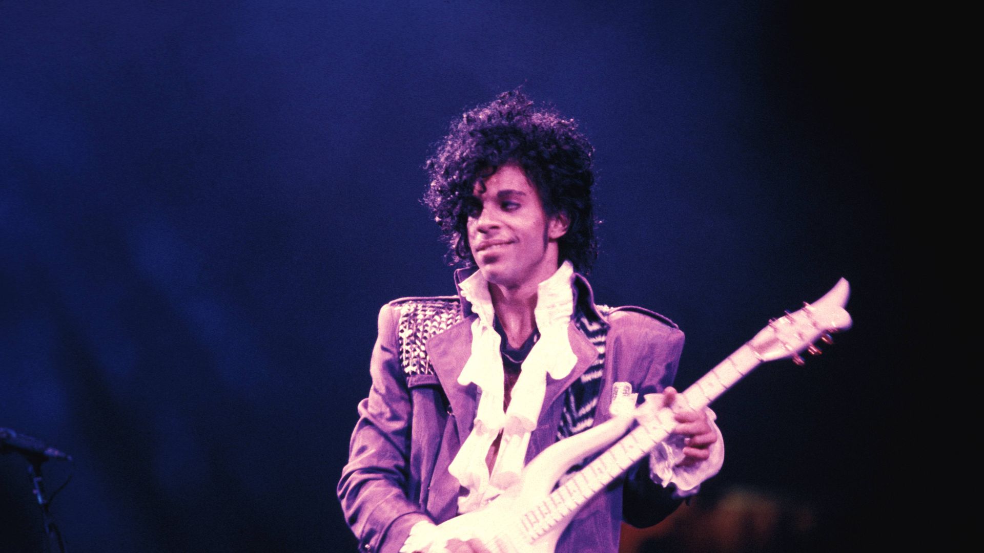 Prince on stage in purple with his guitar