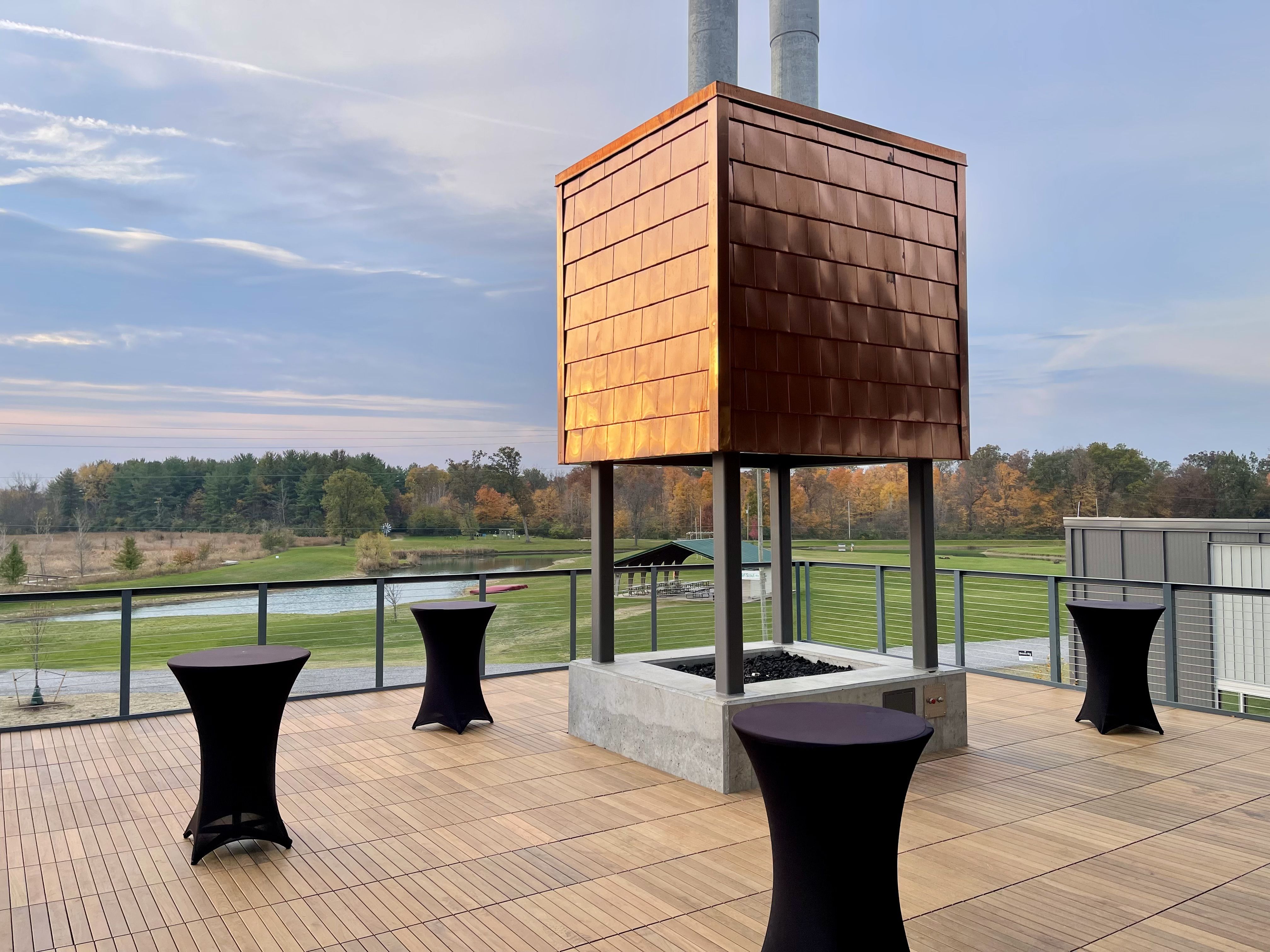 A large gathering space on an outdoor deck with a large fire pit at its center