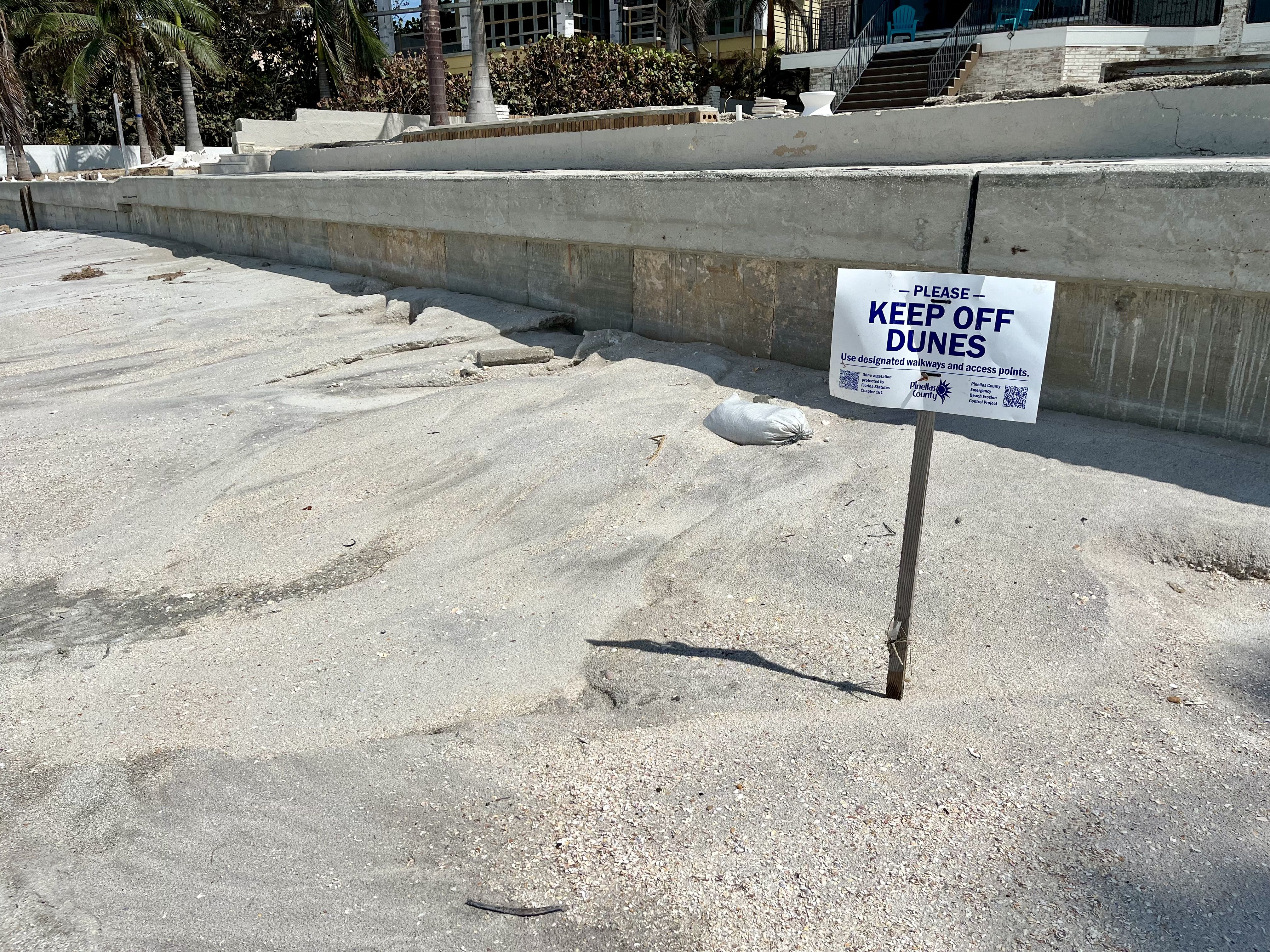 A sign stuck in the sand reads "PLEASE KEEP OFF DUNES."