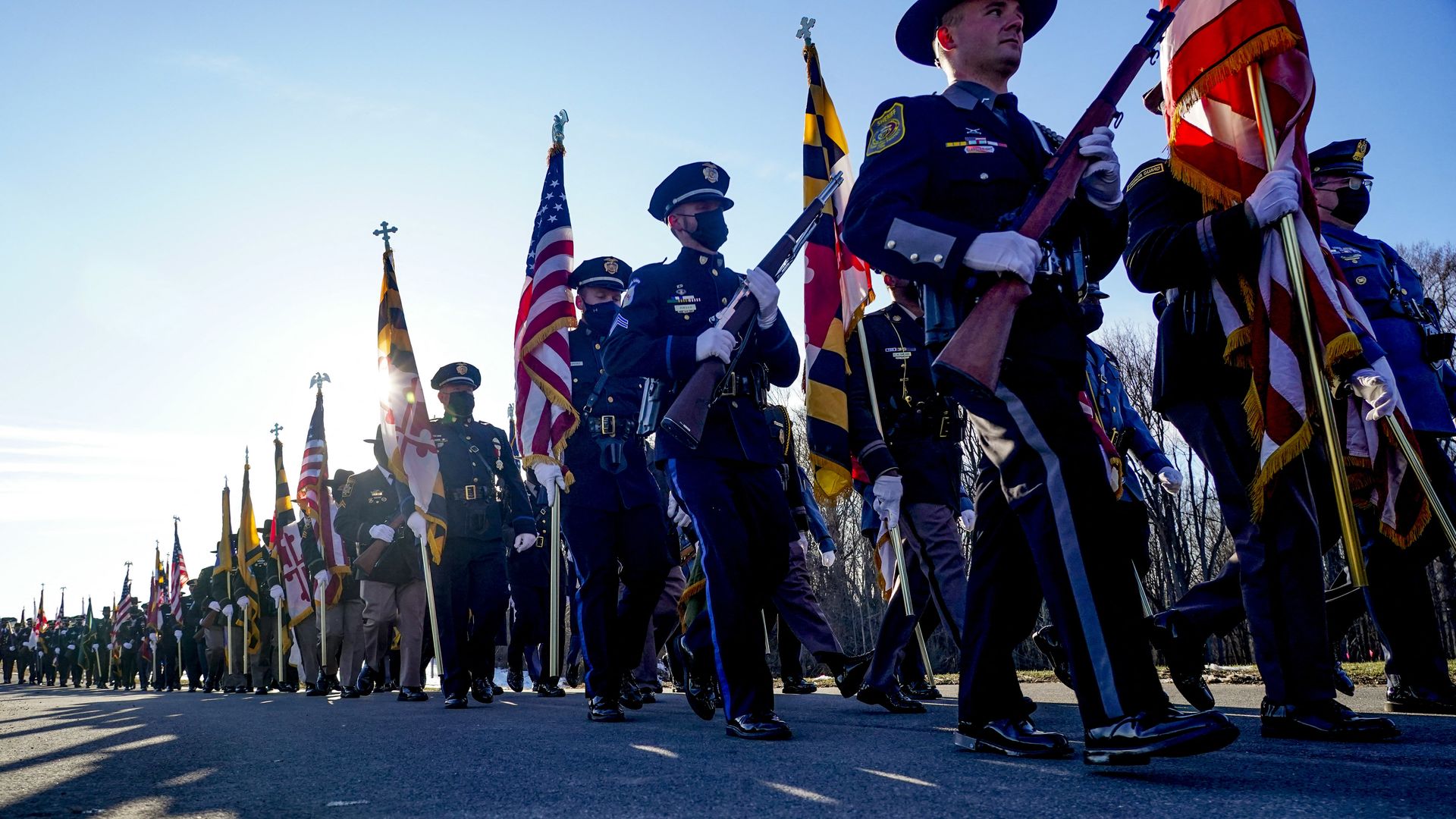 Photo of a line of law enforcement officers in uniform and marching while holding flags