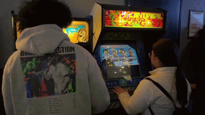 Two people play arcade video games. 