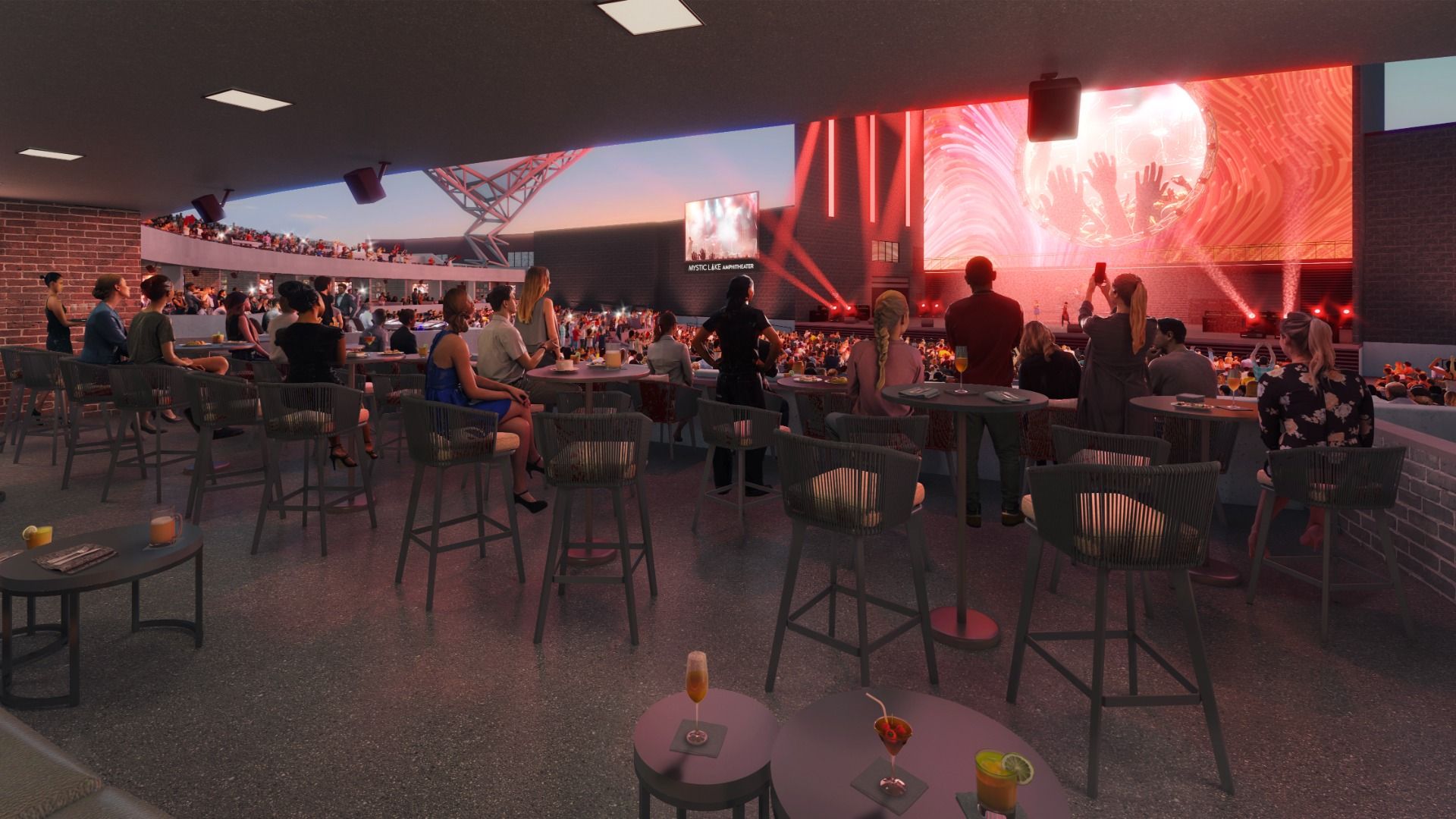 Open-air concert venue with a red-lit stage. Foreground shows round tables with drinks; audience sits on balconies and floor-level chairs, watching a large live performance under dramatic lighting.