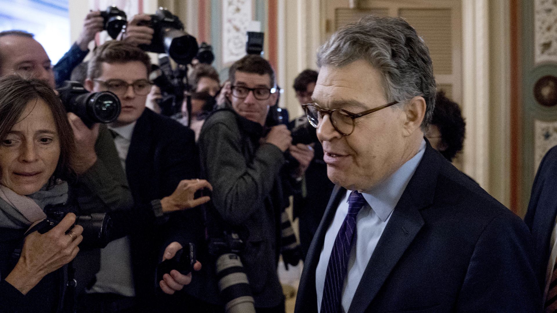 Sen. Al Franken walking past reporters with cameras with his head down. 