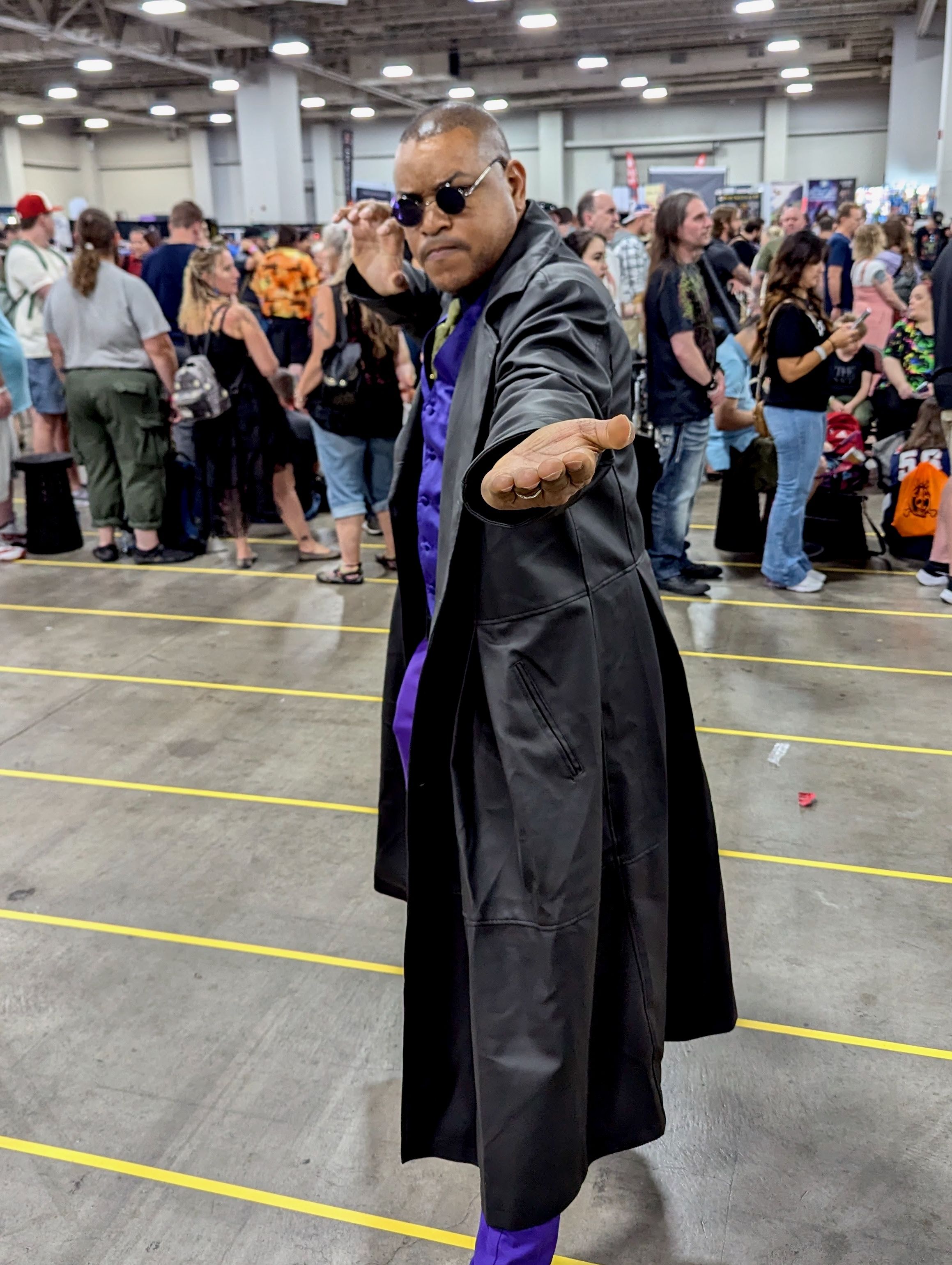 A man dressed as Morpheus from The Matrix, posing in a convention center.