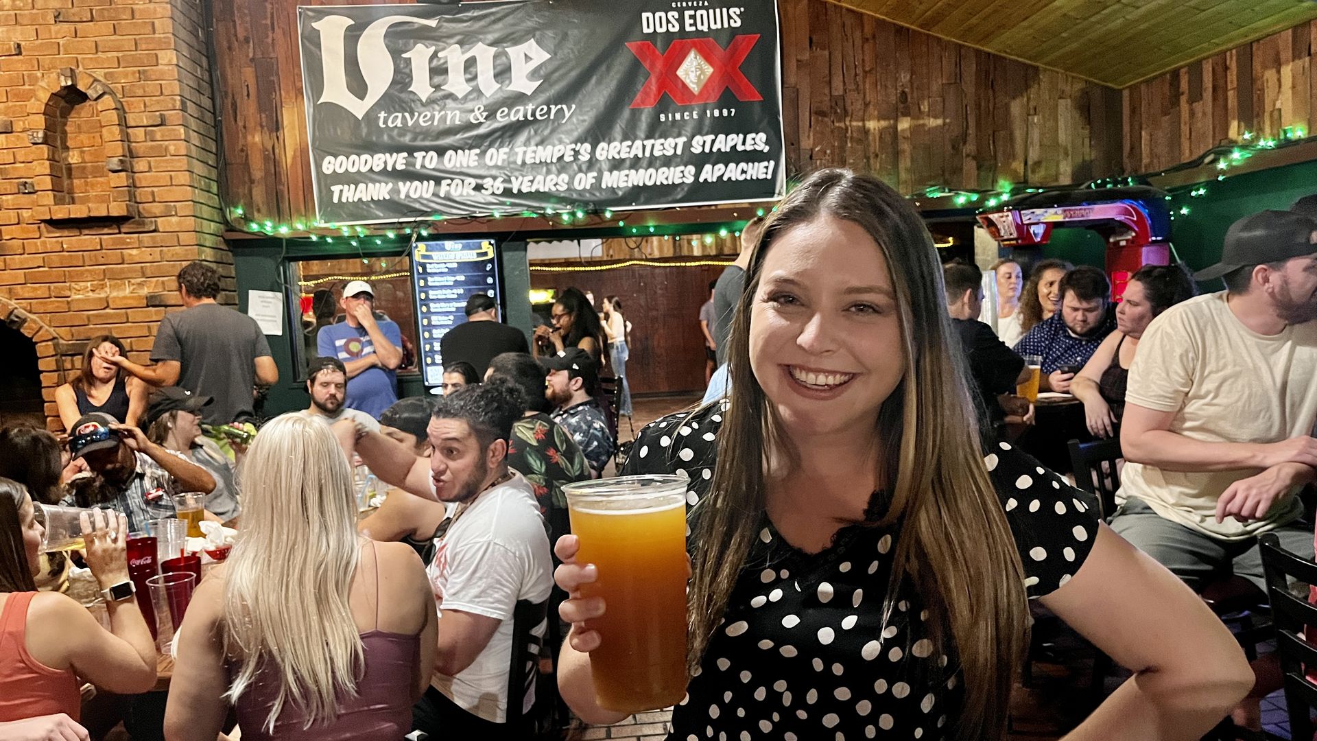 A woman holding a large beer under a sign that says "The Vine."