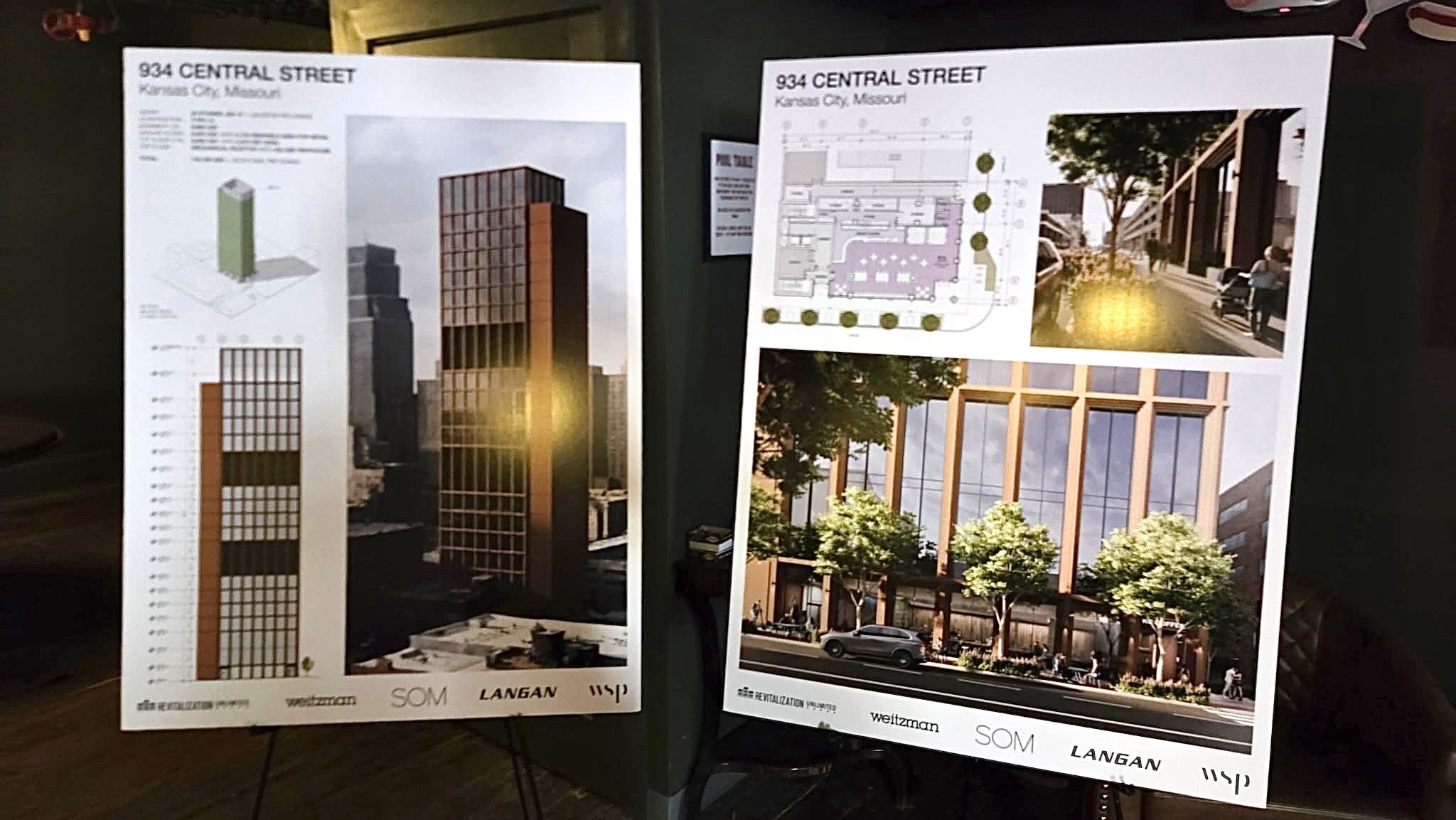 Two large poster boards reading "934 CENTRAL STREET" show architectural designs: left board with tall brown-gray tower renders, right board with a site plan and a street-view photo of a modern building along a tree-lined street.