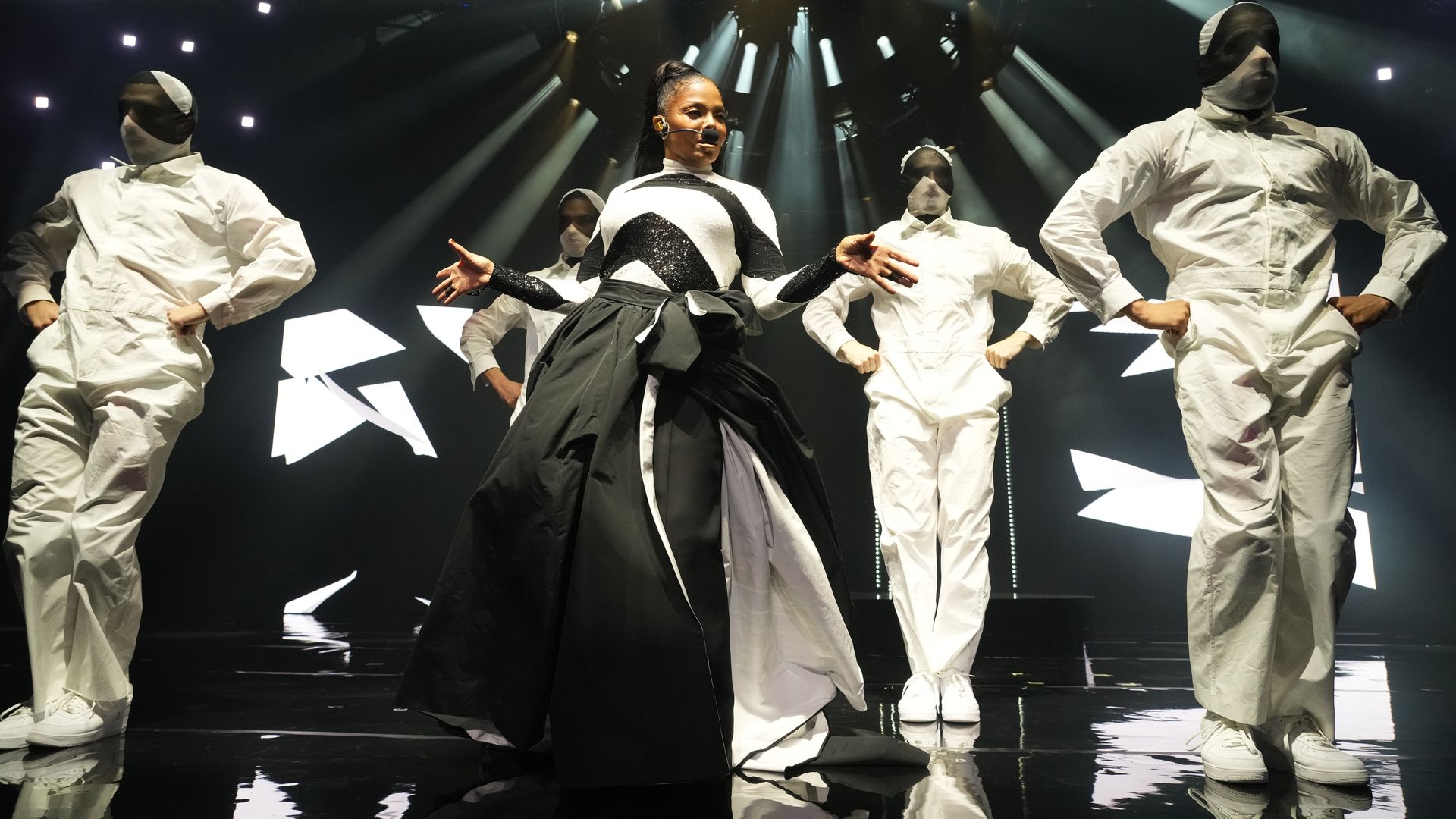 Photo shows Janet Jackson on stage with dancers dressed in white.