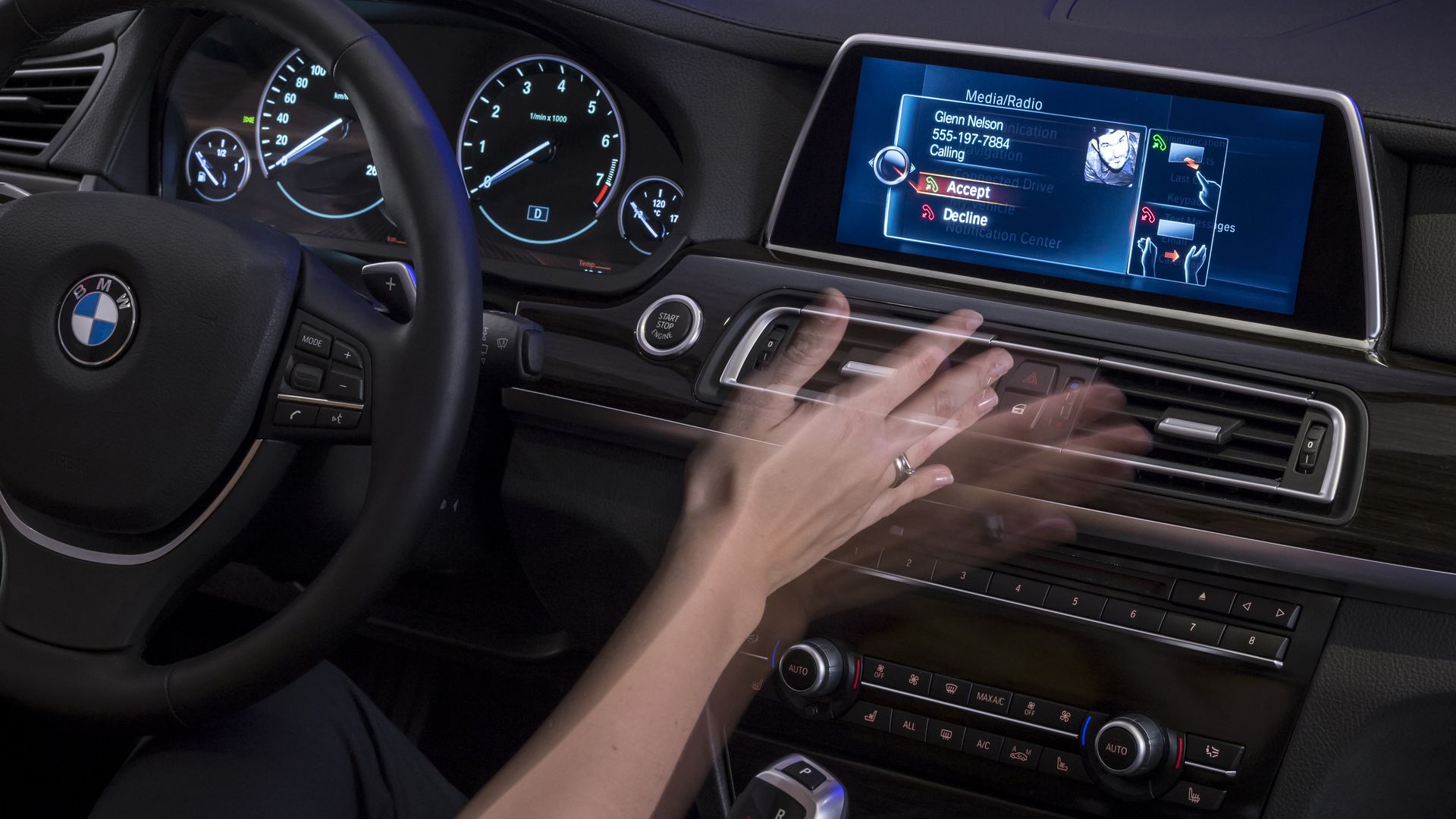 Image of a person's hand waving in front of a BMW car's infotainment system to answer a call. 