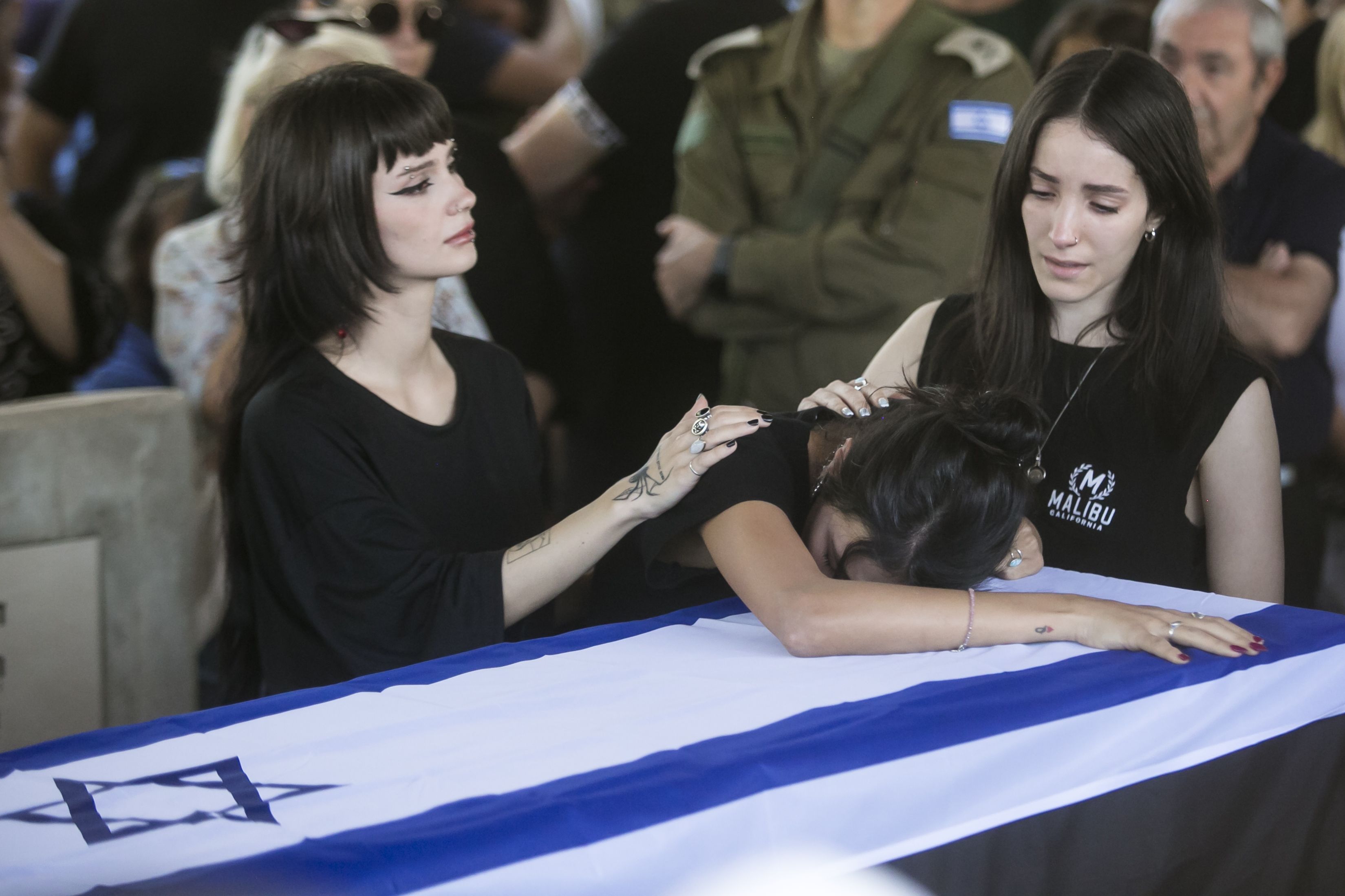 Three women mourn over a casket covered in an Israeli flag. 
