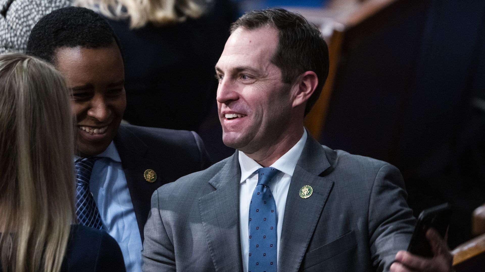 Rep. Jason Crow, wearing a gray suit, speaking with colleagues on the House floor.
