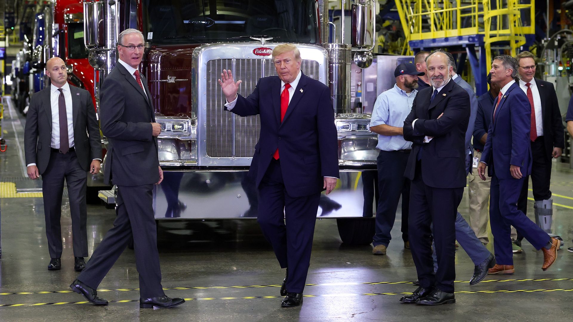 President Trump, PACCAR Inc. CEO R. Preston Feight and U.S. Secretary of Commerce Howard Lutnick walk in front of a truck cab parked indoors.