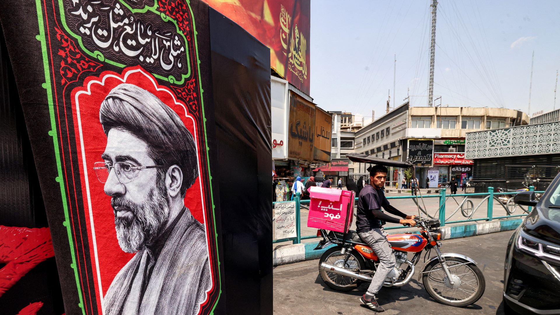 A delivery person rides a motorcycle near an image of Iran's Supreme Leader Mojtaba Khamenei. Photo: Atta Kenare/AFP via Getty Images