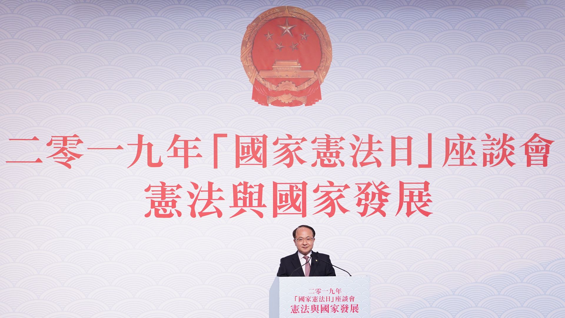 In this image, Wang Zhimin stands behind a podium with Chinese characters behind him