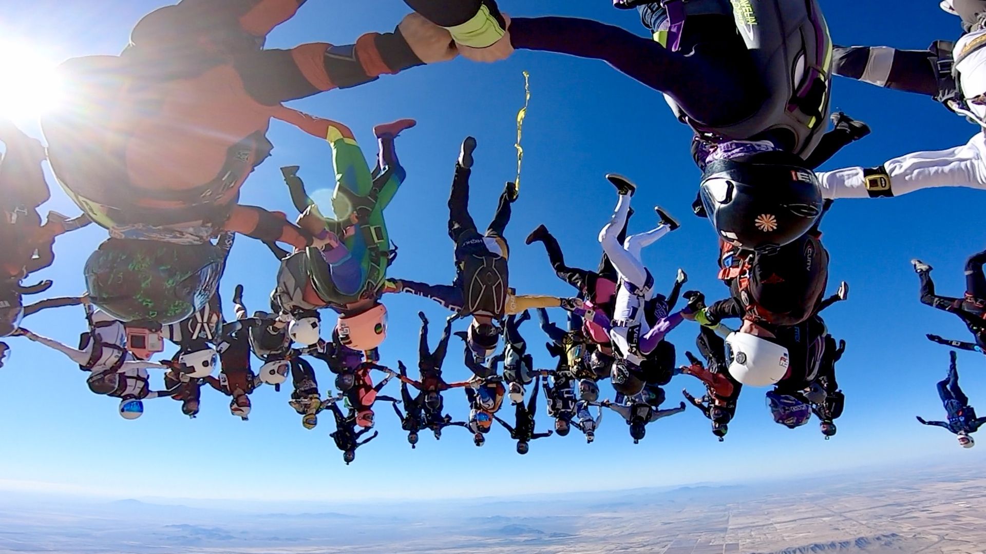 Dozens of skydivers  linking arms while upside down. 