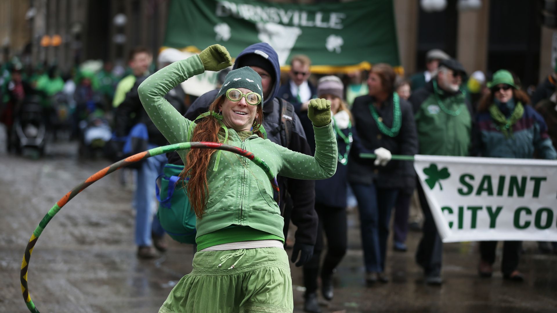 A woman wearing all green hula hooping at a St. Patrick's Day parade.
