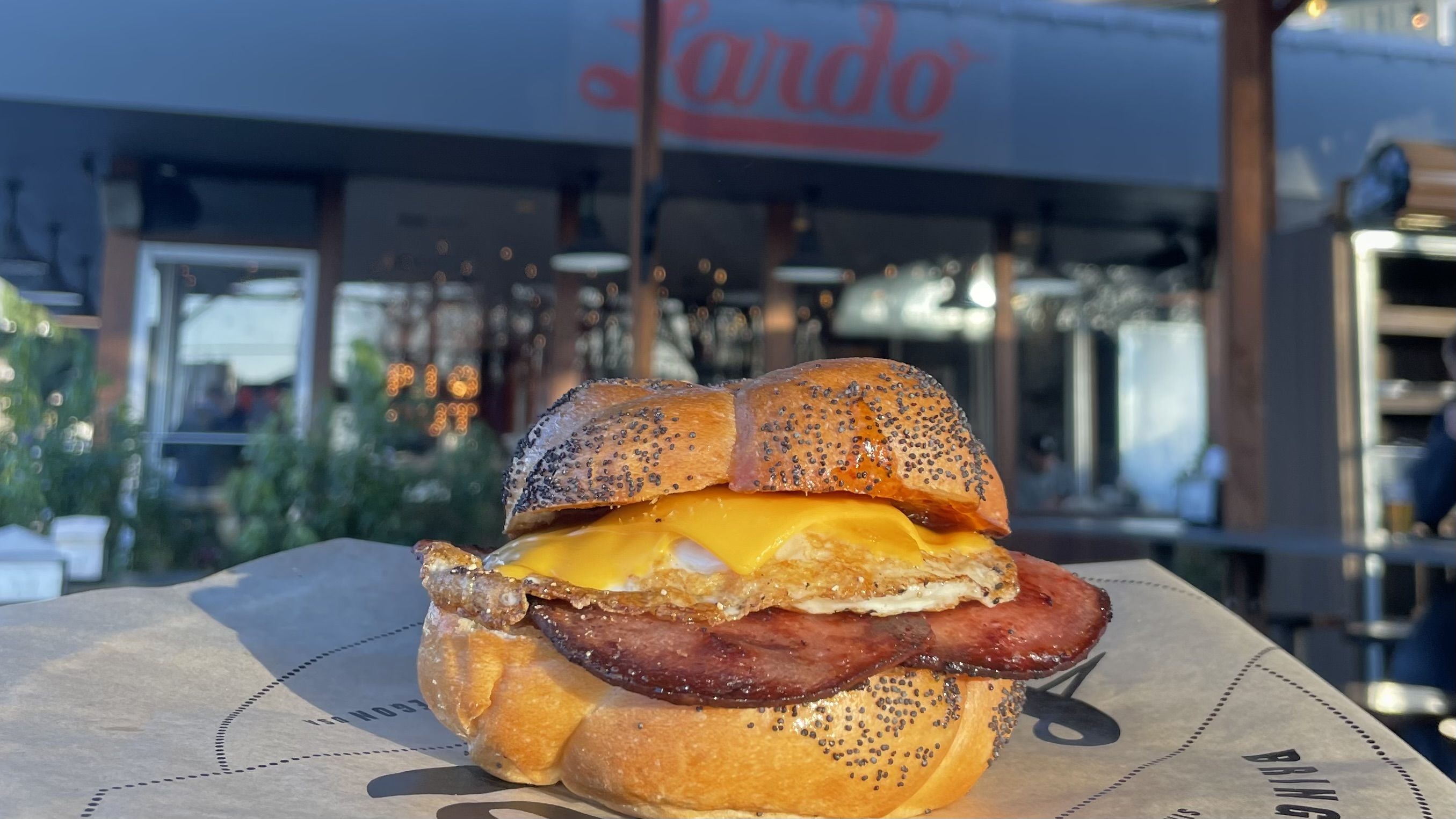 A photo of a sandwich on a paper plate with the signage "Lardo" in the back of the frame.