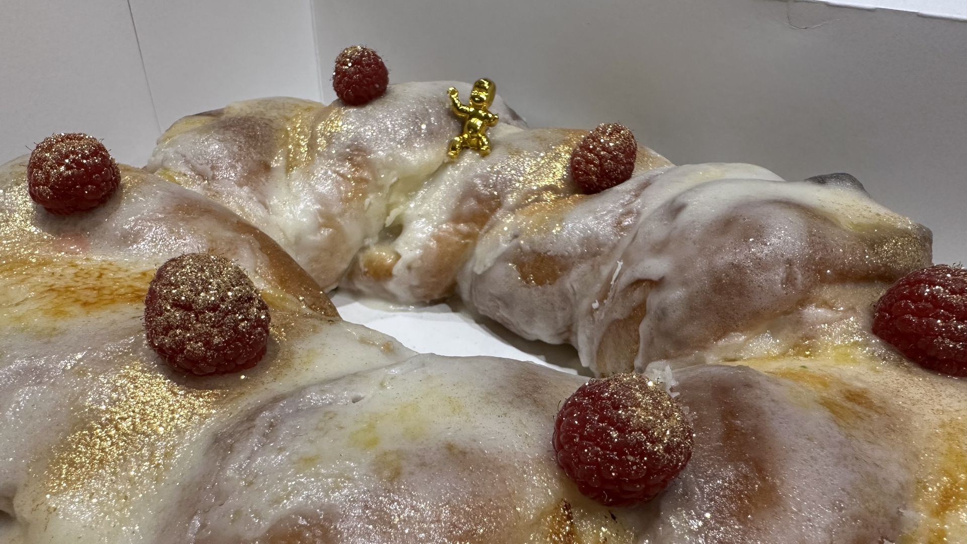 A close-up photo of a king cake that's been topped with gold dust and raspberries. A gold baby sits on top.