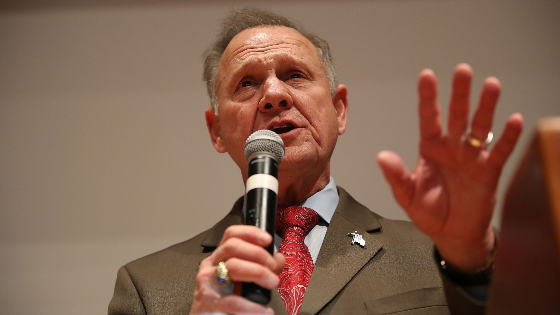 In this image, Roy Moore speaks into a microphone and waves a hand. 